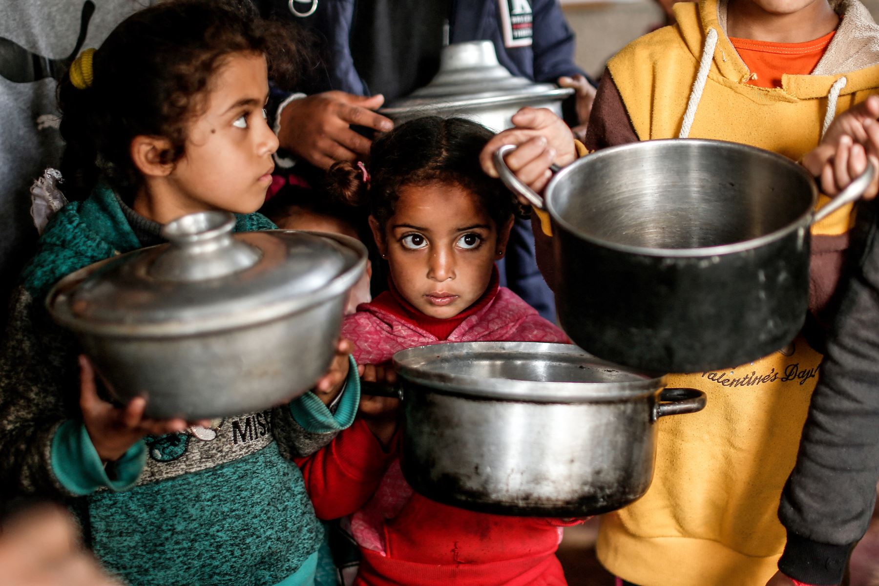 Niños palestinos cargan ollas mientras esperan recibir una comida preparada con ingredientes obtenidos de donantes que desean ayudar a familias necesitadas, en un barrio empobrecido de la ciudad de Gaza. Foto: AFP