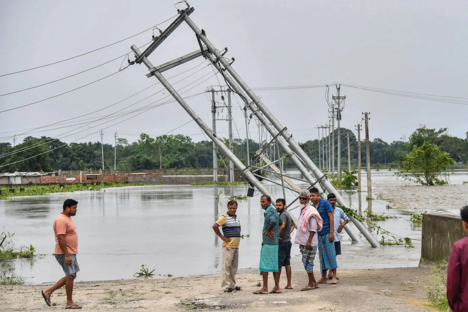 La gente mira los pilares eléctricos volcados que fueron dañados por las inundaciones en el distrito de Rangia de Kamrup, en el estado indio de Assam.
Foto: AFP