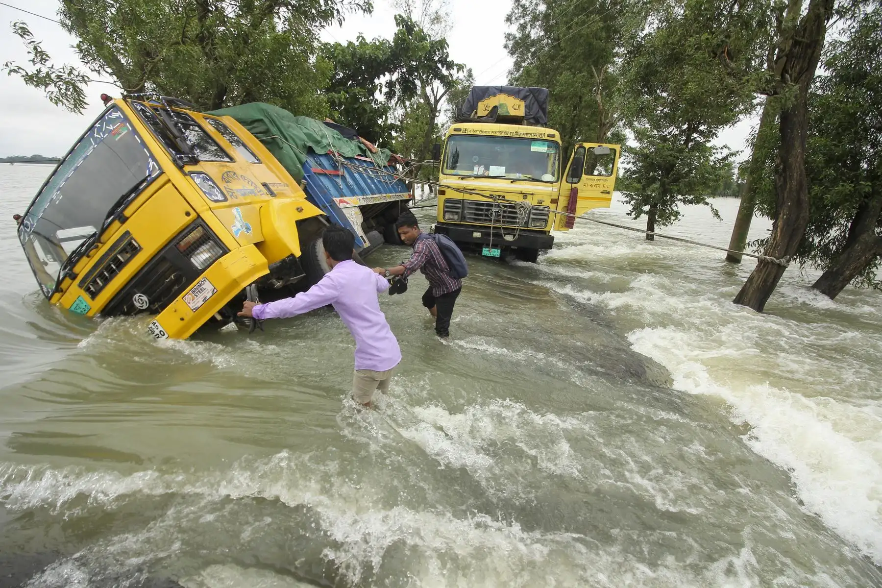 La gente pasa junto a camiones varados en una calle inundada en Sunamganj. Las inundaciones son una amenaza habitual para millones de personas en las zonas bajas de Bangladesh. Foto: AFP