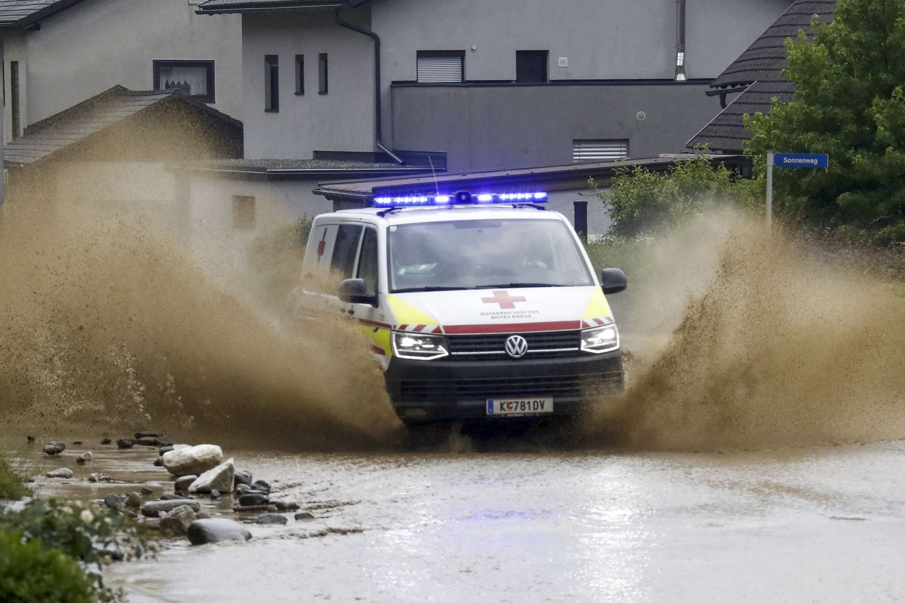 Una camioneta de la cruz roja salpica agua a los costados mientras conduce por una carretera inundada en Treffen, en el distrito de Villach-Land del estado de Carintia, Austria, el 29 de junio de 2022. Foto: AFP