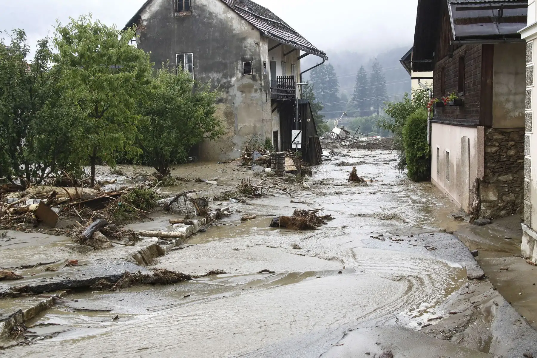 Los escombros y el agua fluyen cuesta abajo en una carretera entre casas en Treffen, en el distrito de Villach-Land del estado de Carintia, Austria, el 29 de junio de 2022. - Los rescatistas intentaban llegar a tres pueblos en el oeste de Austria. Foto: AFP