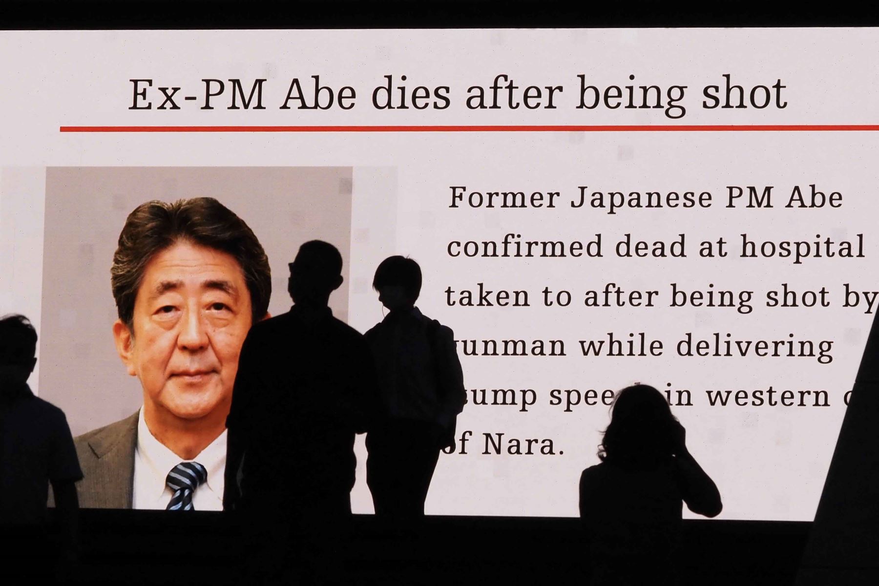 Los peatones caminan cerca a una gran pantalla de video pública que muestra una imagen del ex primer ministro japonés Shinzo Abe en el distrito de Akihabara de Tokio. Abe fue declarado muerto el 8 de julio, confirmó el hospital que lo atendió, luego de que le dispararan. Foto: AFP