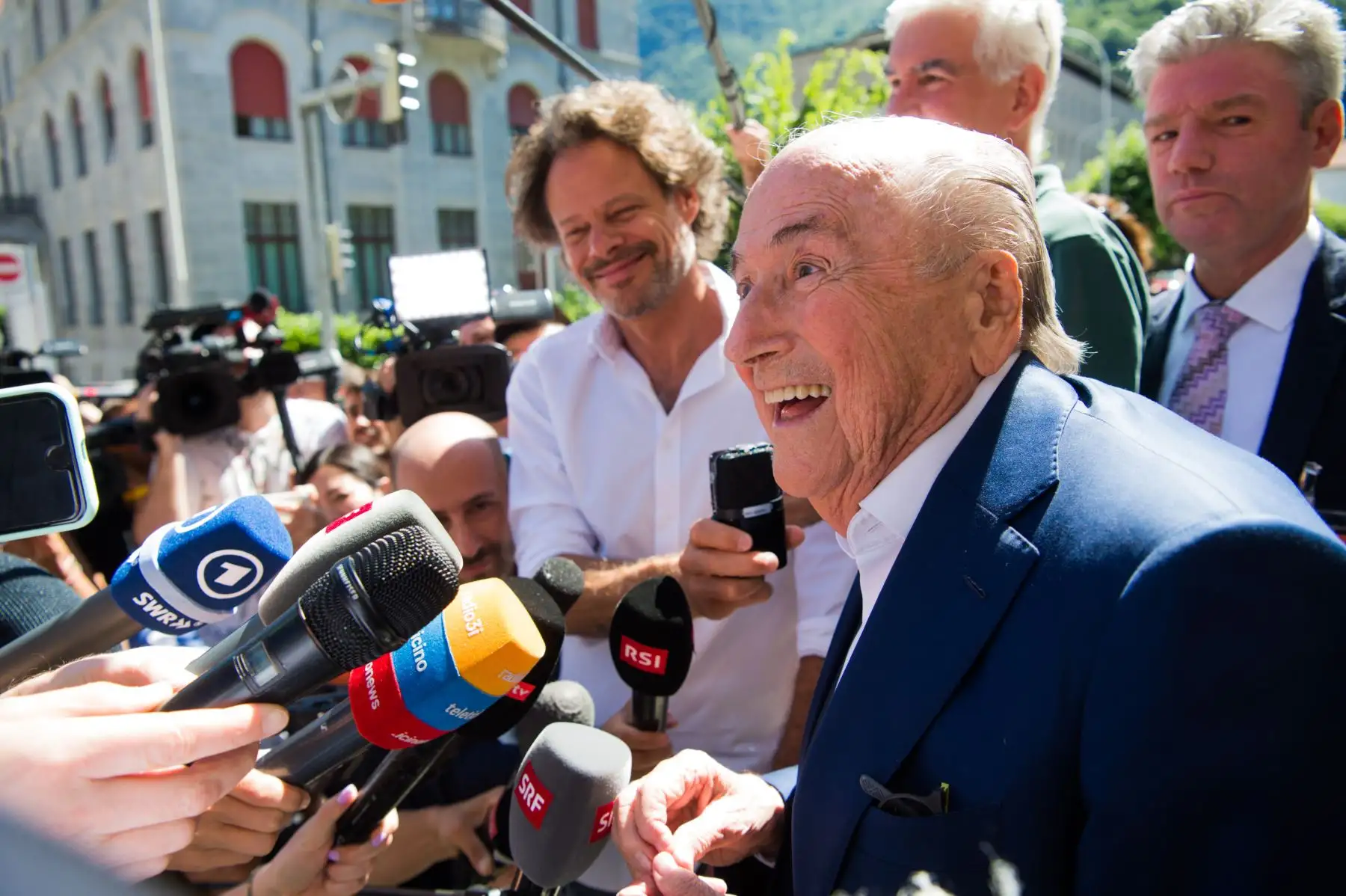 El ex presidente de la FIFA, Joseph Blatter, rodeado de representantes de los medios de comunicación, saluda a la prensa este viernes frente al Tribunal Penal Federal Suizo tras conocerse el veredicto de absolución en Bellinzona. La Fiscalía Federal acusó de fraude al ex presidente de la FIFA, Joseph Blatter, y al ex presidente de la UEFA, Michel Platini, por un pago sospechoso de dos millones. 
Foto: EFE