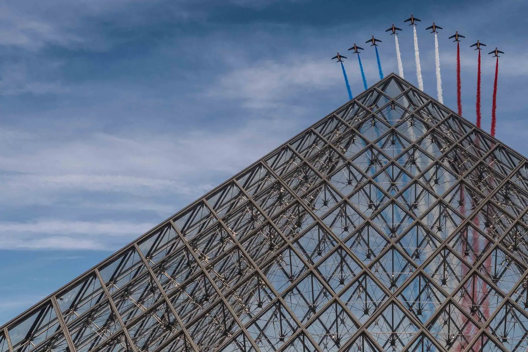 El equipo de vuelo acrobático de élite francés "Patrouille de France" suelta humo con los colores de la bandera francesa mientras sobrevuelan la Pirámide del Louvre diseñada por el arquitecto chino Ieoh Ming Pei durante el desfile militar del Día de la Bastilla en París. Foto: AFP