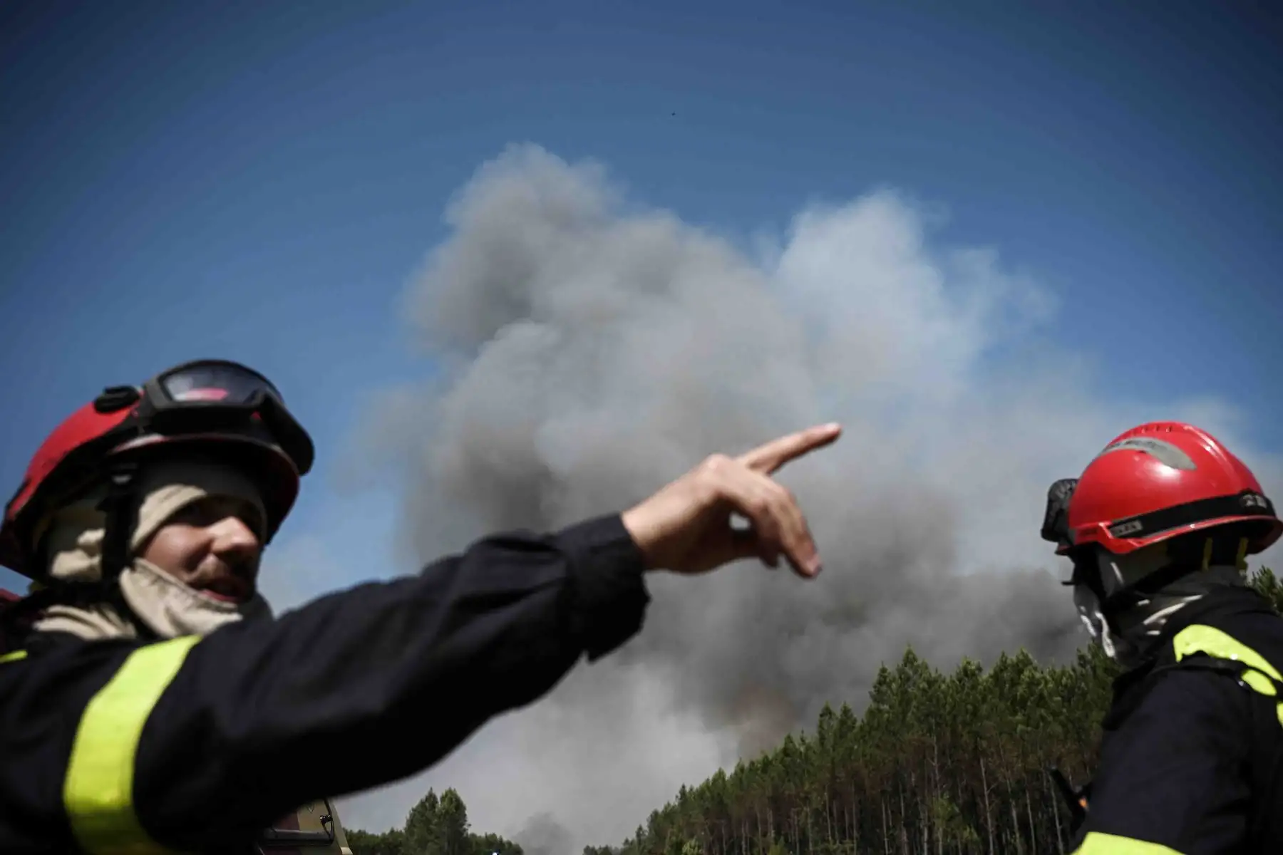 Bomberos se paran en una carretera mientras se ve humo denso en el fondo durante los incendios forestales cerca de la ciudad de Origne, en el suroeste de Francia. Foto: AFP
