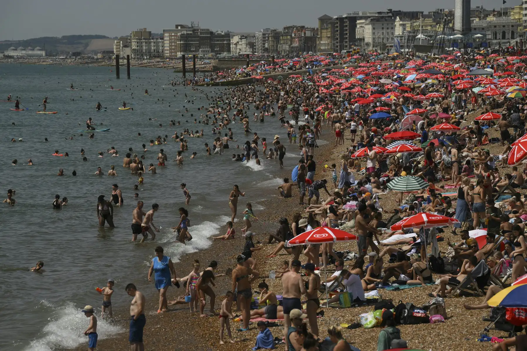 Los bañistas se sientan al sol en la playa y reman en el mar en Brighton, sur de Inglaterra. Foto: AFP