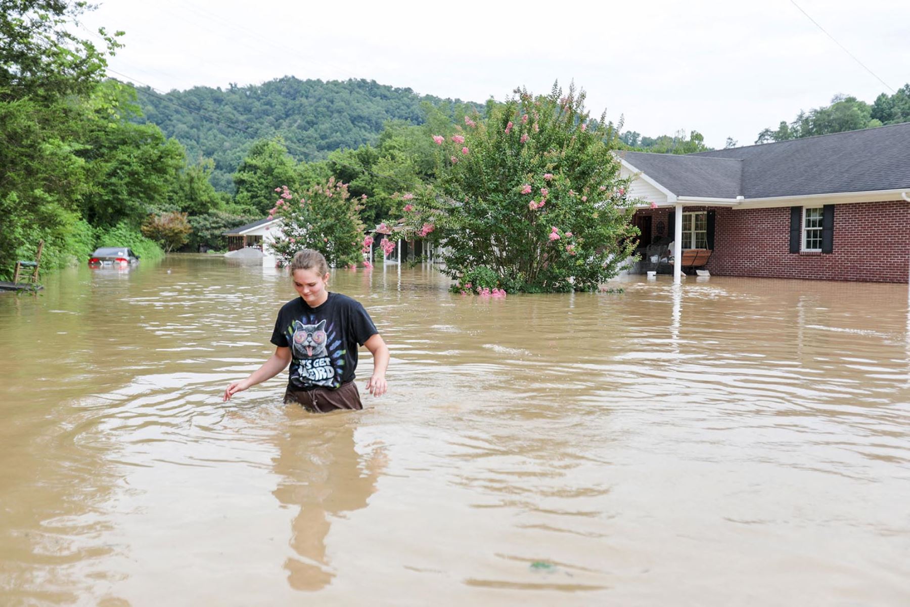 Una joven mujer camina con el agua hasta la cintura junto a una casa inundada por el río Kentucky en Jackson, Kentucky, el 28 de julio del 2022. Foto: AFP