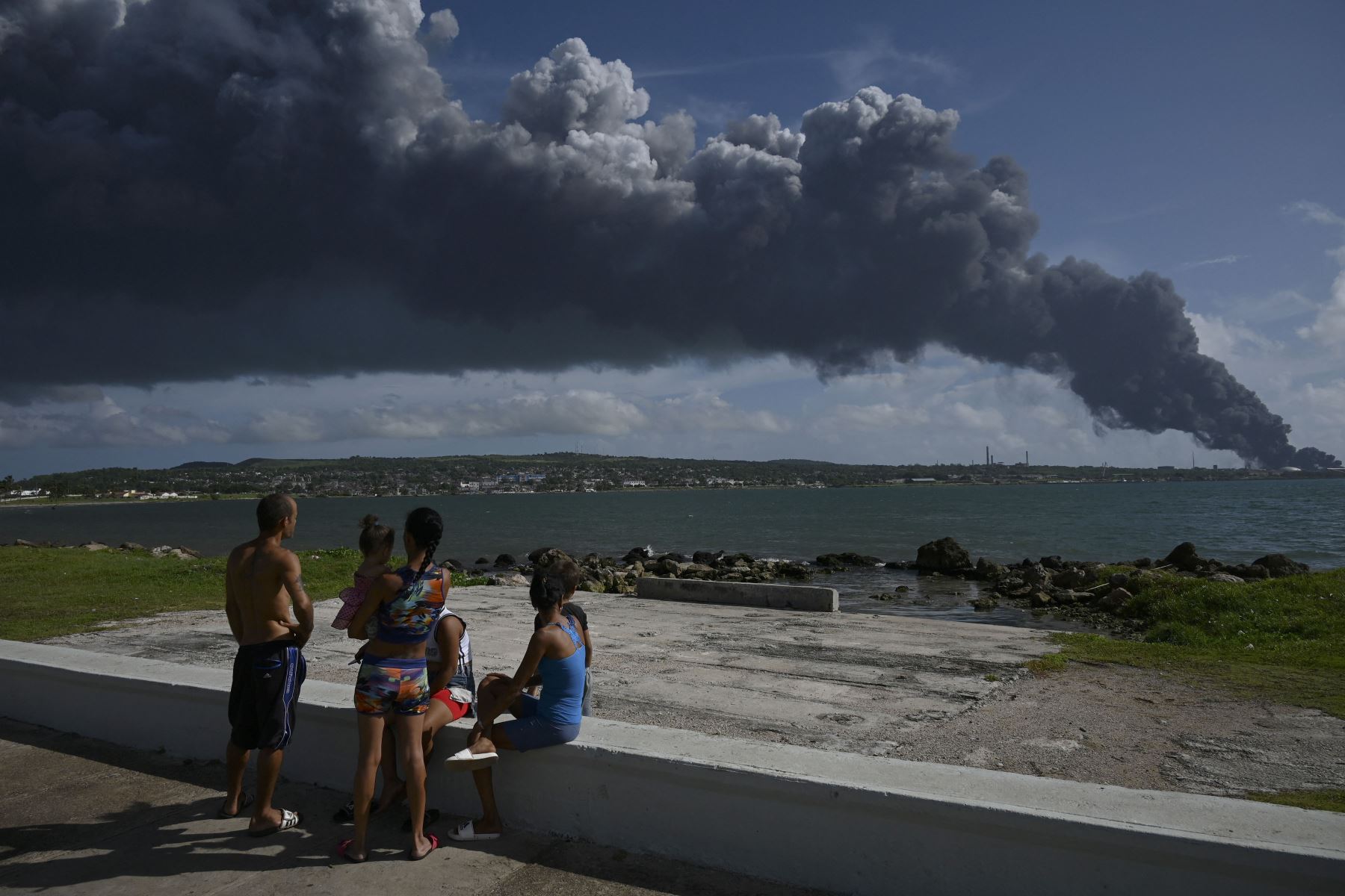 La gente mira el humo negro de un tanque de petróleo en llamas en Matanzas, Cuba. El fuego causado por un rayo el viernes en un depósito de combustible en Matanzas, en el oeste de Cuba, se extendió a un segundo tanque en la madrugada de este sábado.
Foto: AFP