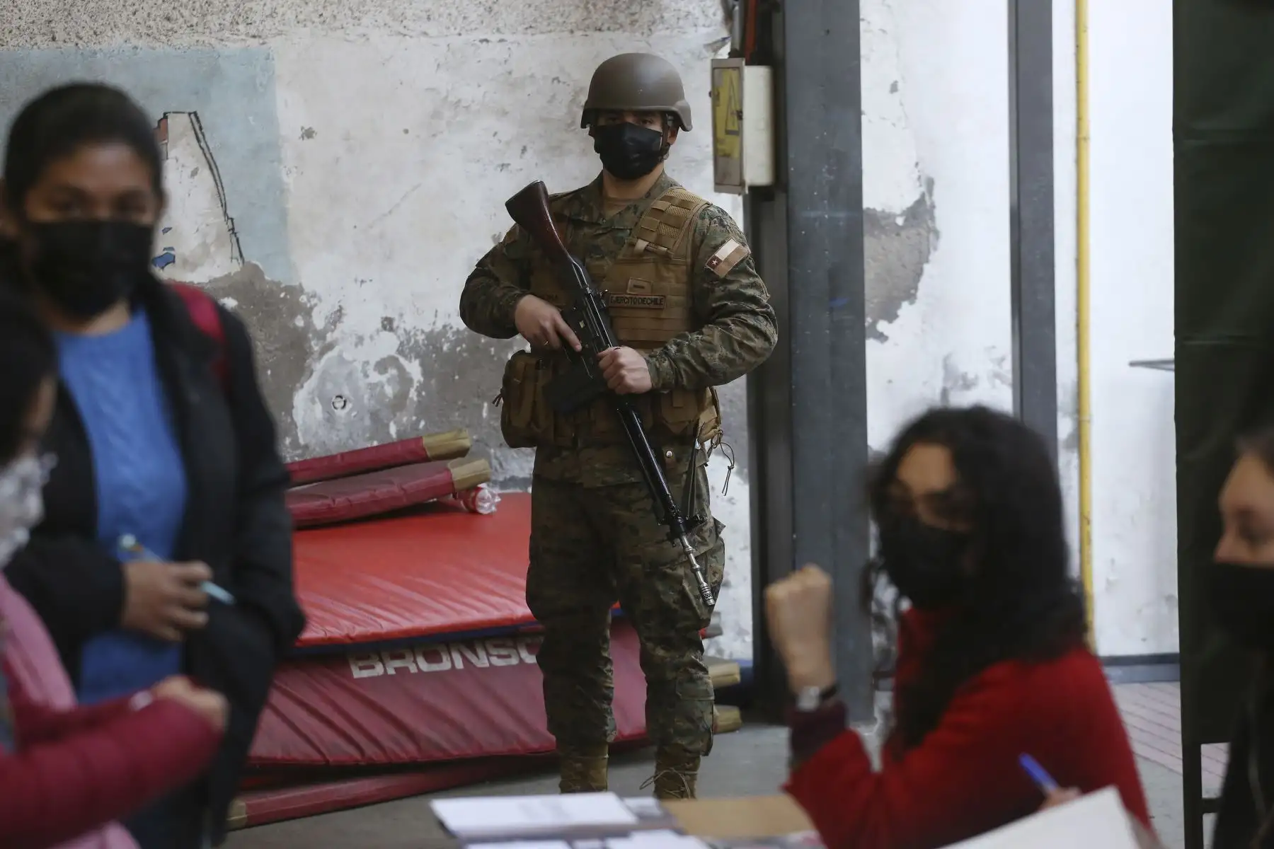 Un soldado presta guardia mientras varios ciudadanos se acercan a votar el plebiscito constitucional hoy, en un colegio electoral en el Instituto Superior de Comercio, en Santiago (Chile). Cerca de 3.000 centros de votación abren este domingo en Chile para dar inicio a una de las votaciones más importantes de su historia reciente, en la que más de 15,1 millones chilenos decidirán si aprueban o rechazan la propuesta de nueva Constitución. Foto: EFE