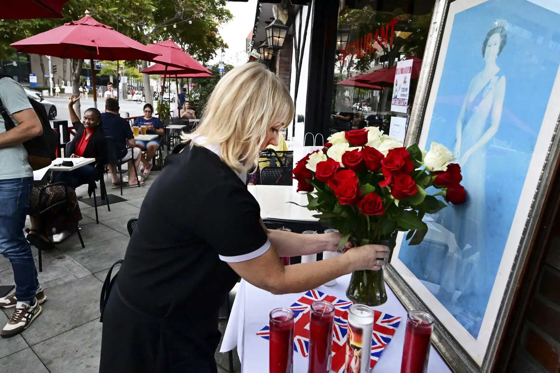Christine McIntosh coloca un ramo de rosas en una Union Jack junto a un retrato de la difunta reina Isabel II frente a un pub británico en Santa Mónica, California. Foto: AFP