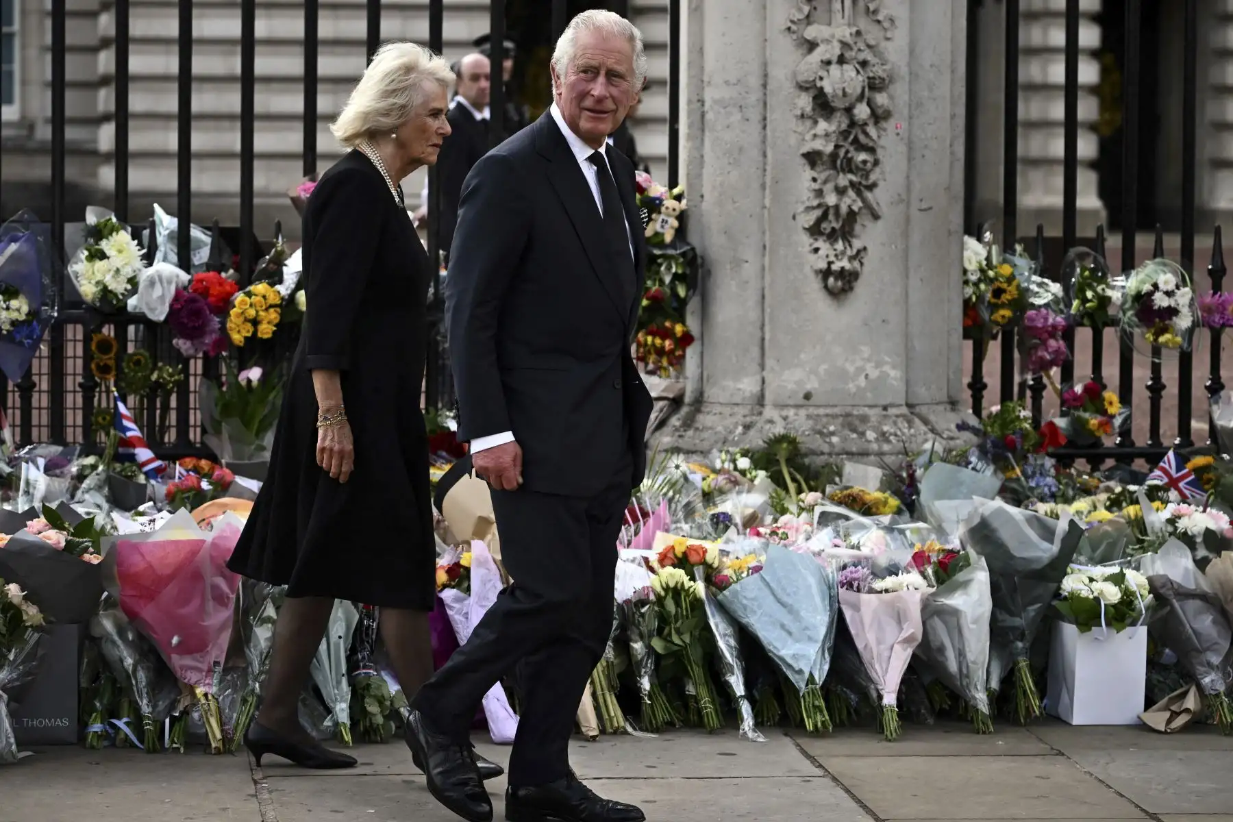 El rey Carlos III de Gran Bretaña y Camila, la reina consorte, caminan frente a los tributos florales que quedan afuera del Palacio de Buckingham en Londres, el 9 de septiembre de 2022, un día después de que la reina Isabel II muriera a la edad de 96 años. Foto: AFP