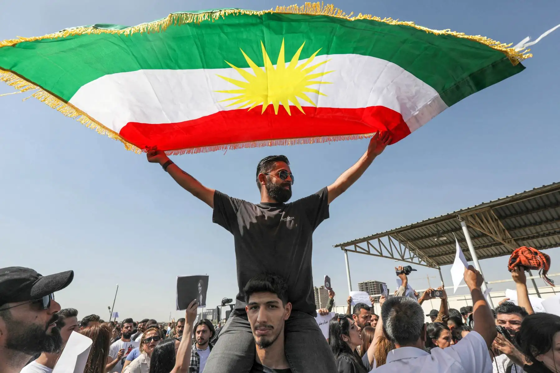 Un hombre ondea una bandera kurda mientras se sienta sobre los hombros de otro durante una manifestación que denuncia la muerte de Mahsa Amini, de 22 años, quien murió mientras estaba bajo la custodia de las autoridades iraníes, a manos de kurdos iraquíes e iraníes frente a las oficinas de la ONU. Foto: AFP