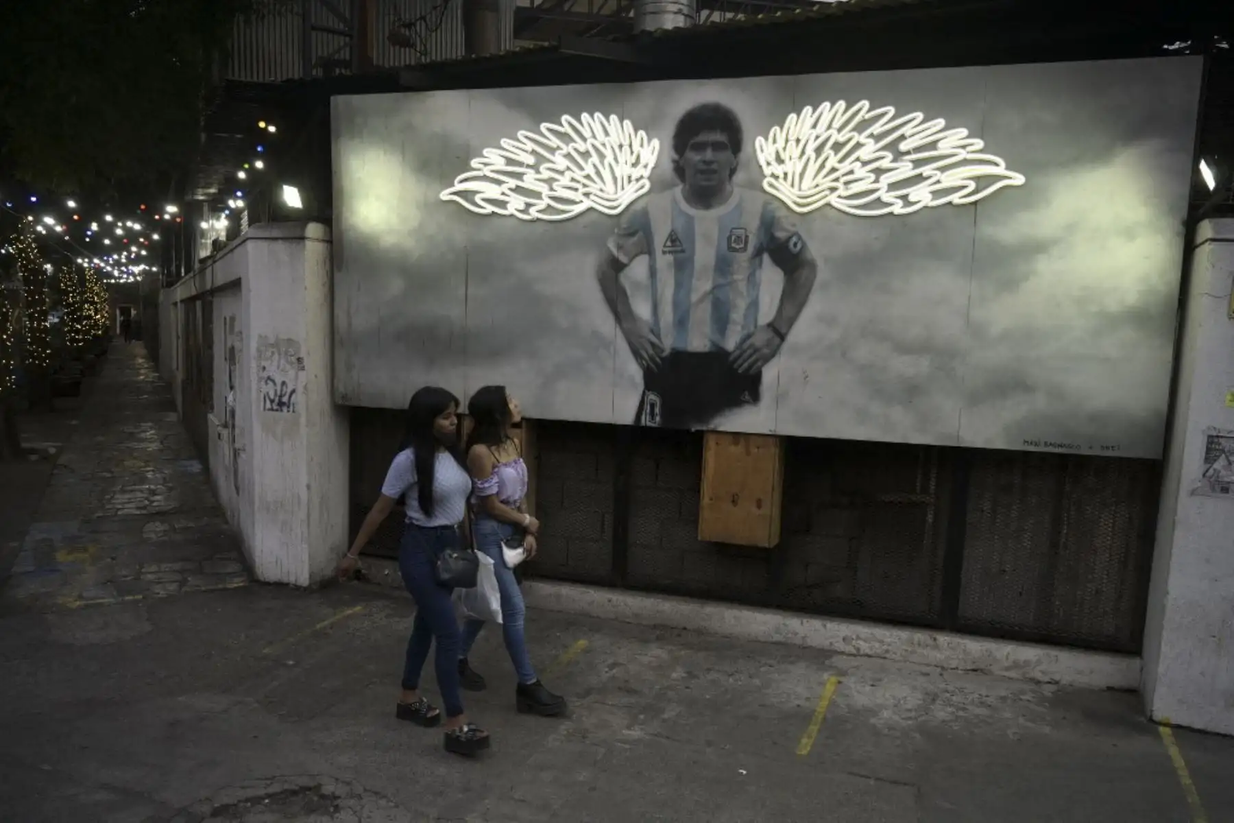 Dos mujeres pasan frente a un mural que representa a la estrella del fútbol argentino Diego Maradona decorado con alas de neón realizadas por los artistas Maximiliano Bagnasco y Dreier Salamanca Vargas, afuera de un restaurante en Buenos Aires. El 30 de octubre marca el 62º aniversario del cumpleaños de la difunta leyenda del fútbol.

Foto: AFP