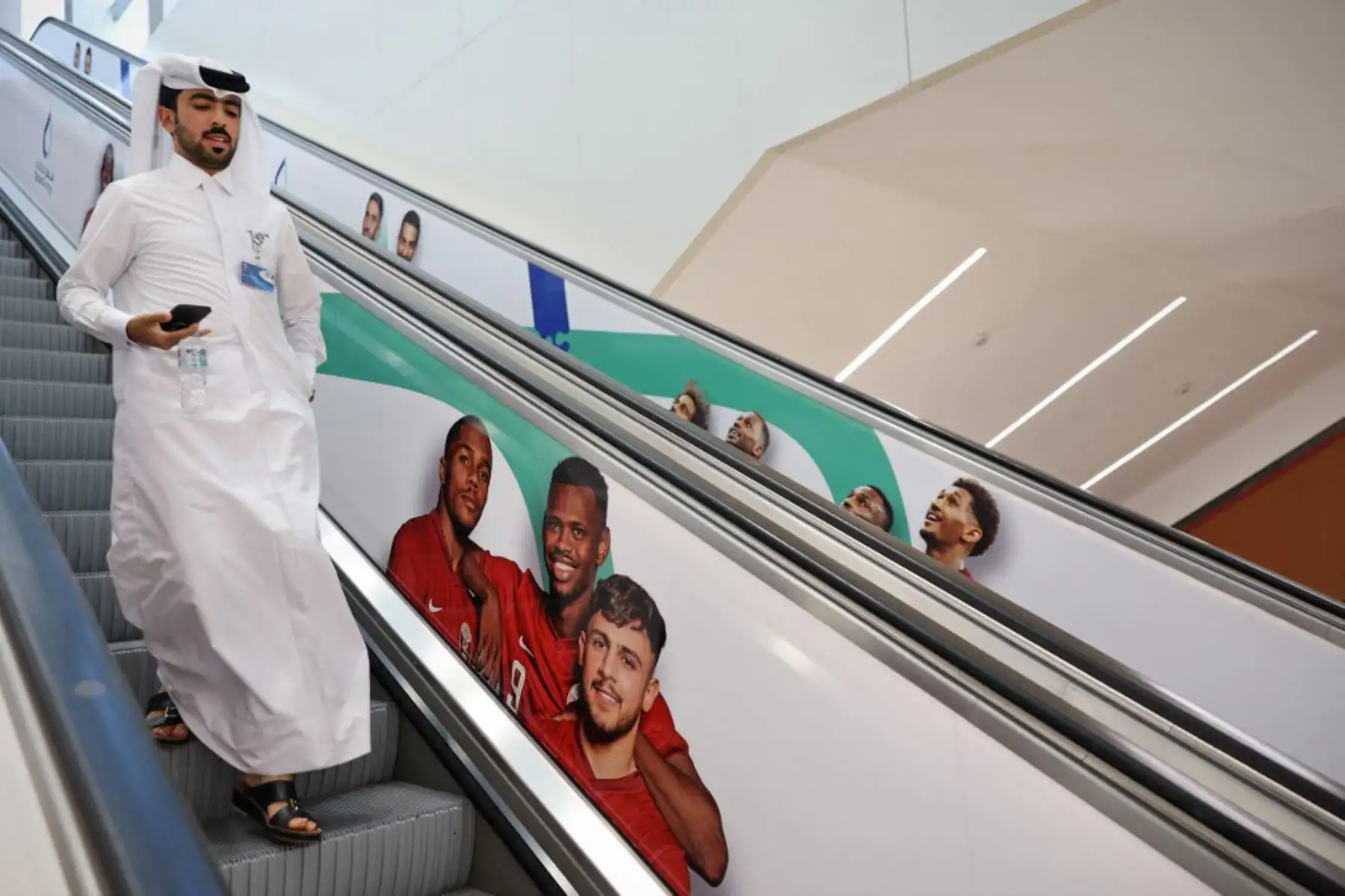 Un hombre baja por la escalera mecánica pasando imágenes de los jugadores de fútbol de Qatar en la estación de metro de West Bay en Doha, antes del torneo de fútbol de la Copa Mundial. Foto: AFP