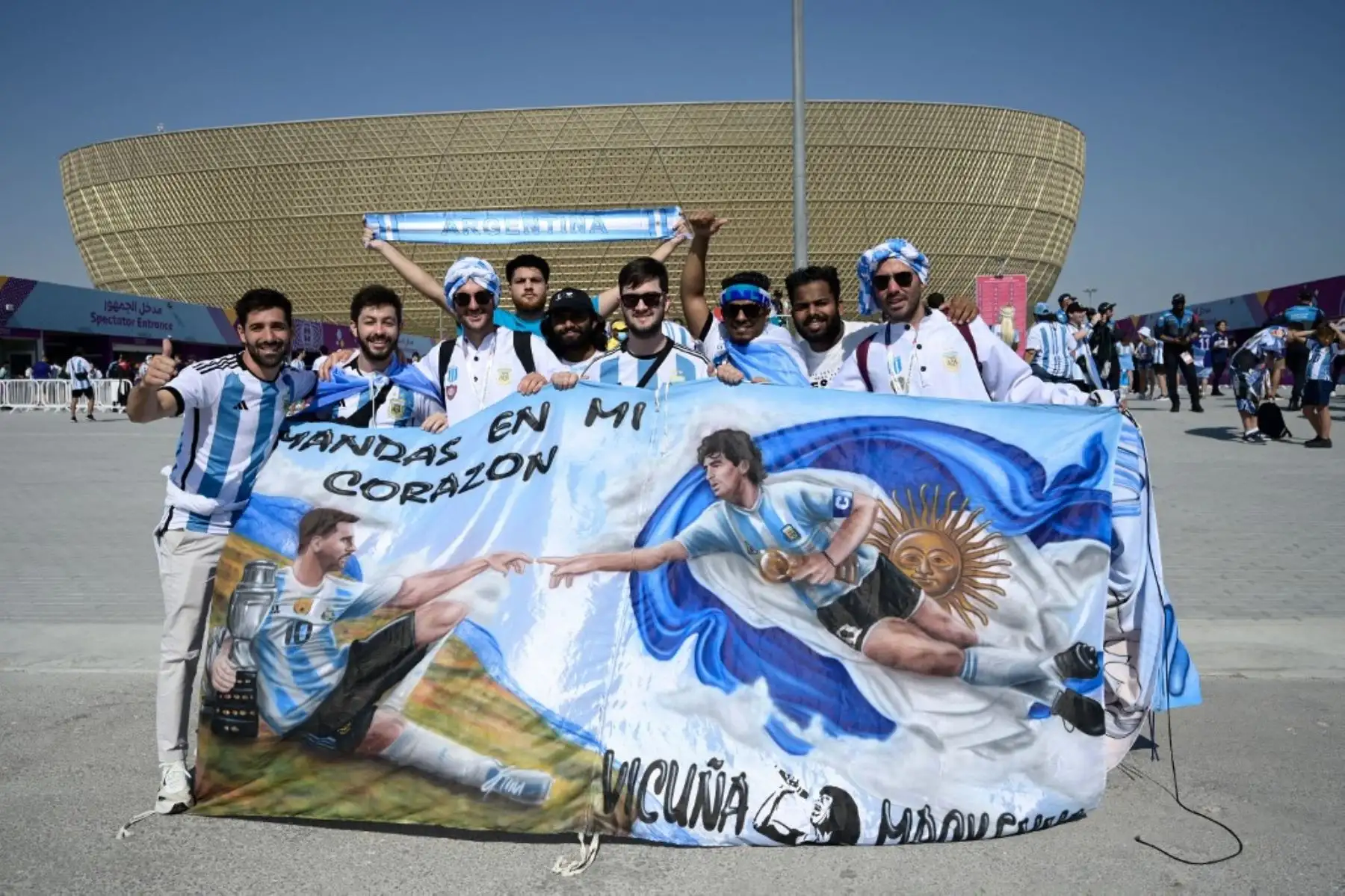 Los simpatizantes de Argentina posan para fotos sosteniendo una bandera que representa al delantero argentino Lionel Messi  y la leyenda del fútbol Diego Maradona fuera del estadio antes del inicio del partido de fútbol del Grupo C de la Copa Mundial Catar 2022 entre Argentina y Arabia Saudita. Foto: EFE