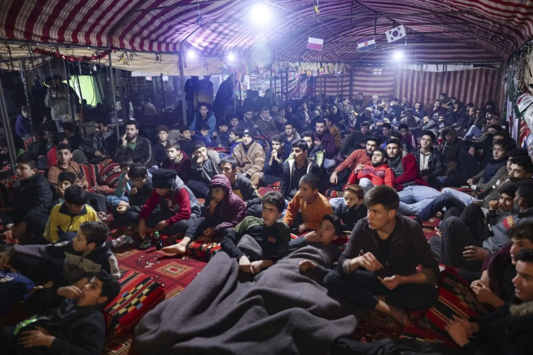 Hombres y niños sirios desplazados ven el partido de fútbol entre Marruecos y Portugal, durante el torneo de la Copa del Mundo de Catar 2022, dentro de una gran carpa instalada por voluntarios de una organización humanitaria para los aficionados en el campamento de Barisha, en la parte norte del territorio controlado por los rebeldes

Foto: AFP