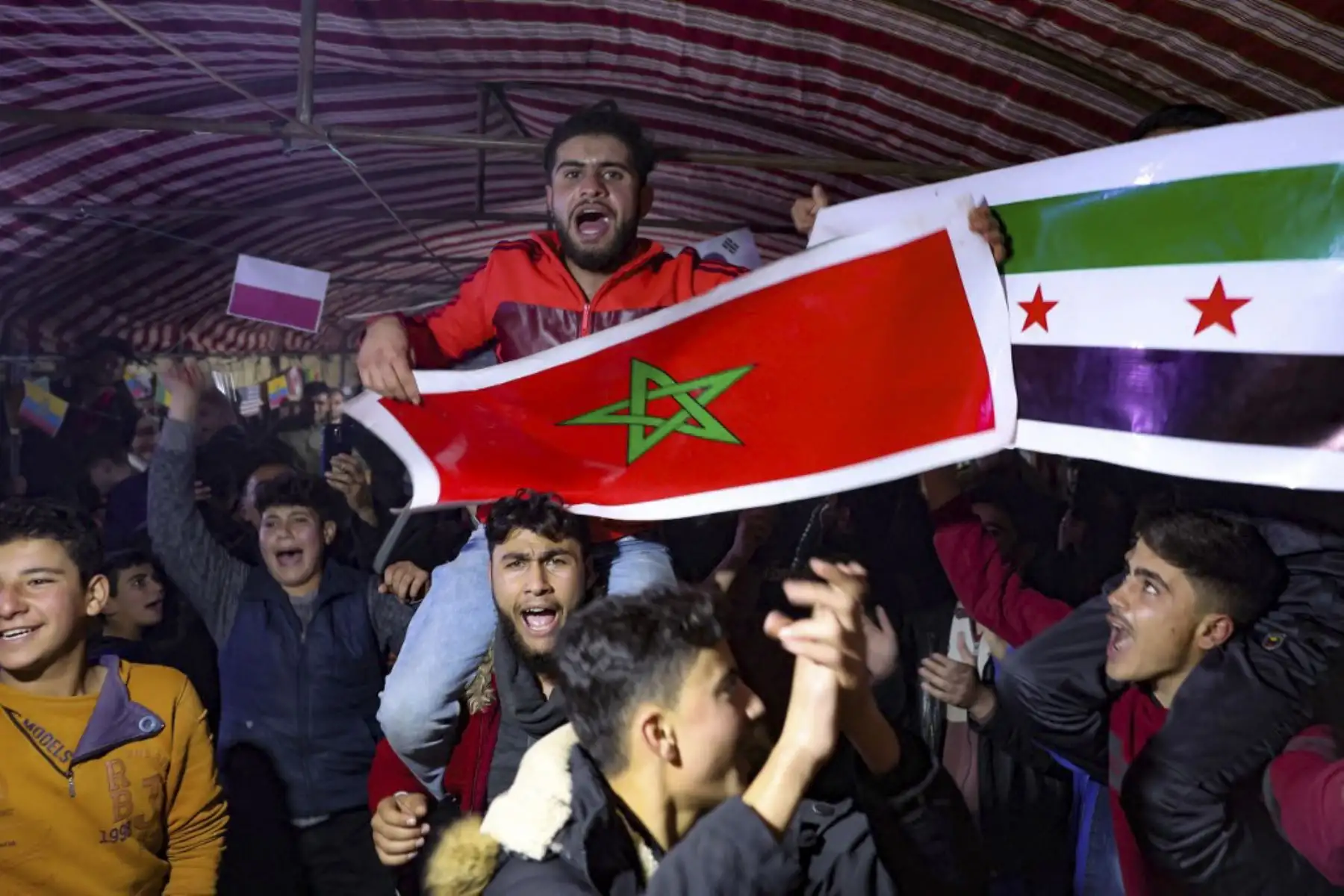 Desplazados sirios ven el partido de fútbol entre Marruecos y Portugal, durante el torneo de la Copa del Mundo de Catar 2022, dentro de una gran carpa instalada por voluntarios de una organización humanitaria para los aficionados en el campamento de Barisha, en la parte norte del territorio controlado por los rebeldes

Foto: AFP