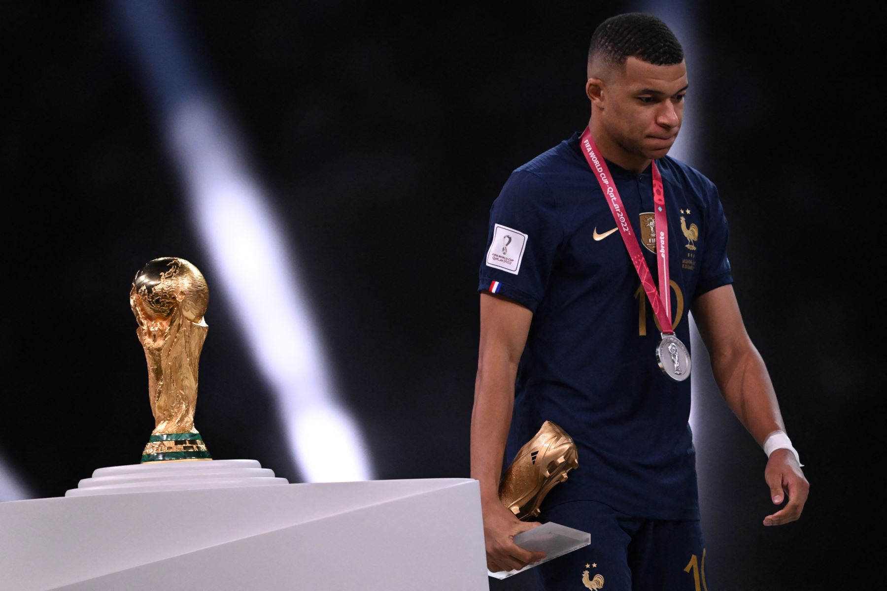 El delantero francés Kylian Mbappe luce abatido mientras pasa junto al Trofeo de la Copa Mundial de la FIFA durante la ceremonia de entrega de trofeos después de que Francia perdiera el partido de fútbol final de la Copa Mundial Qatar 2022 entre Argentina y Francia en el Estadio Lusail en Lusail, al norte de Doha, el 18 de diciembre de 2022.
Foto: AFP