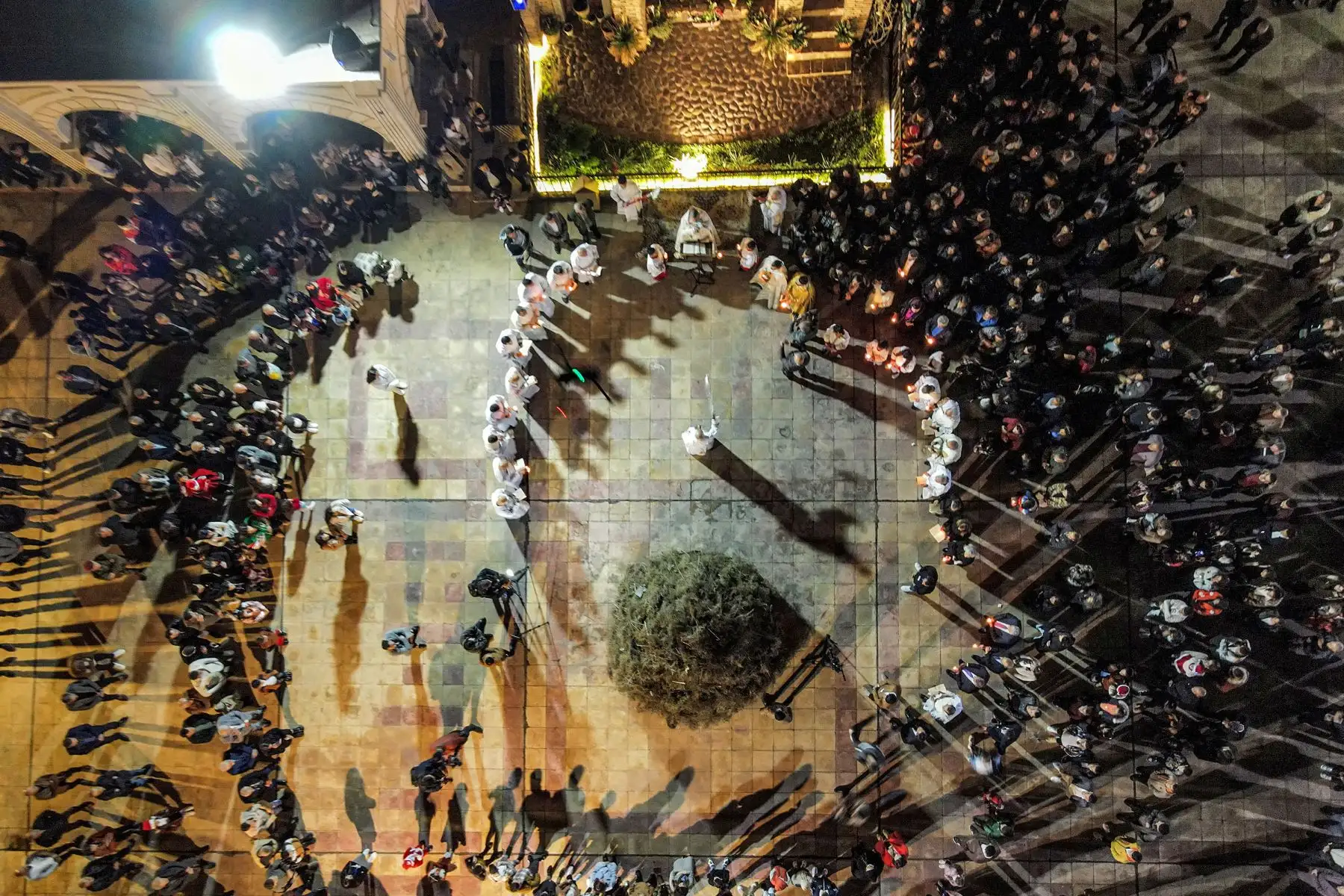 Esta vista aérea muestra a un diácono balanceando un incensario ante un sacerdote mientras los fieles se reúnen antes de encender una hoguera en el patio de la Iglesia Católica Siria de la Inmaculada Concepción (Al-Tahira-l-Kubra), en la ciudad predominantemente cristiana de Qaraqosh en Irak ( Baghdeda).Foto: AFP