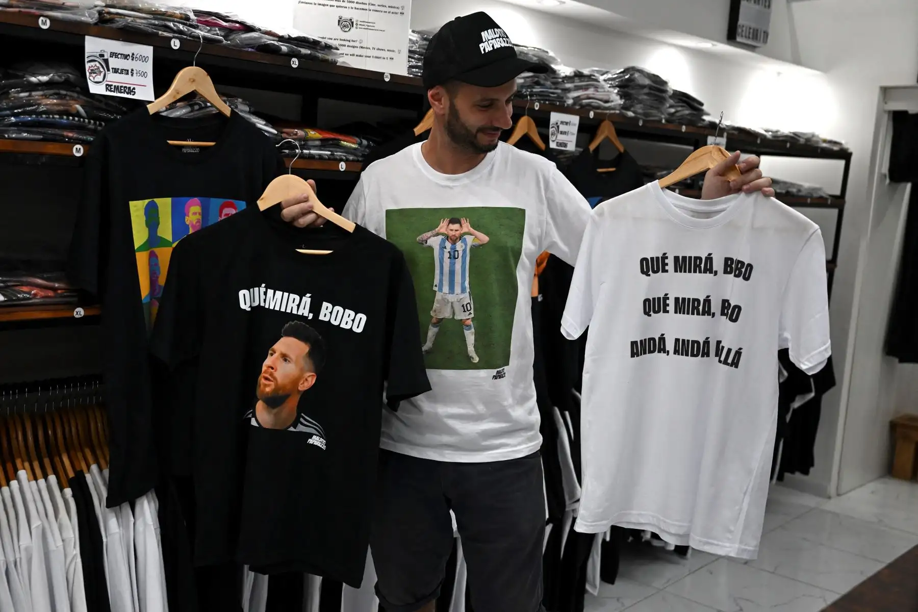 Un hombre sostiene camisetas con una imagen del delantero argentino Lionel Messi y una frase que dice "¿Qué estás mirando, tonto?". en una tienda de Buenos Aires, el 12 de diciembre de 2022. El orgullo de los hinchas argentinos al ver por fin a Lionel Messi en modo carismático líder desató un furor comercial al vender productos con una pendenciera frase suya tras vencer a Holanda (4-3 en los penales) en los cuartos de final del Mundial de Qatar-2022.

Foto: AFP