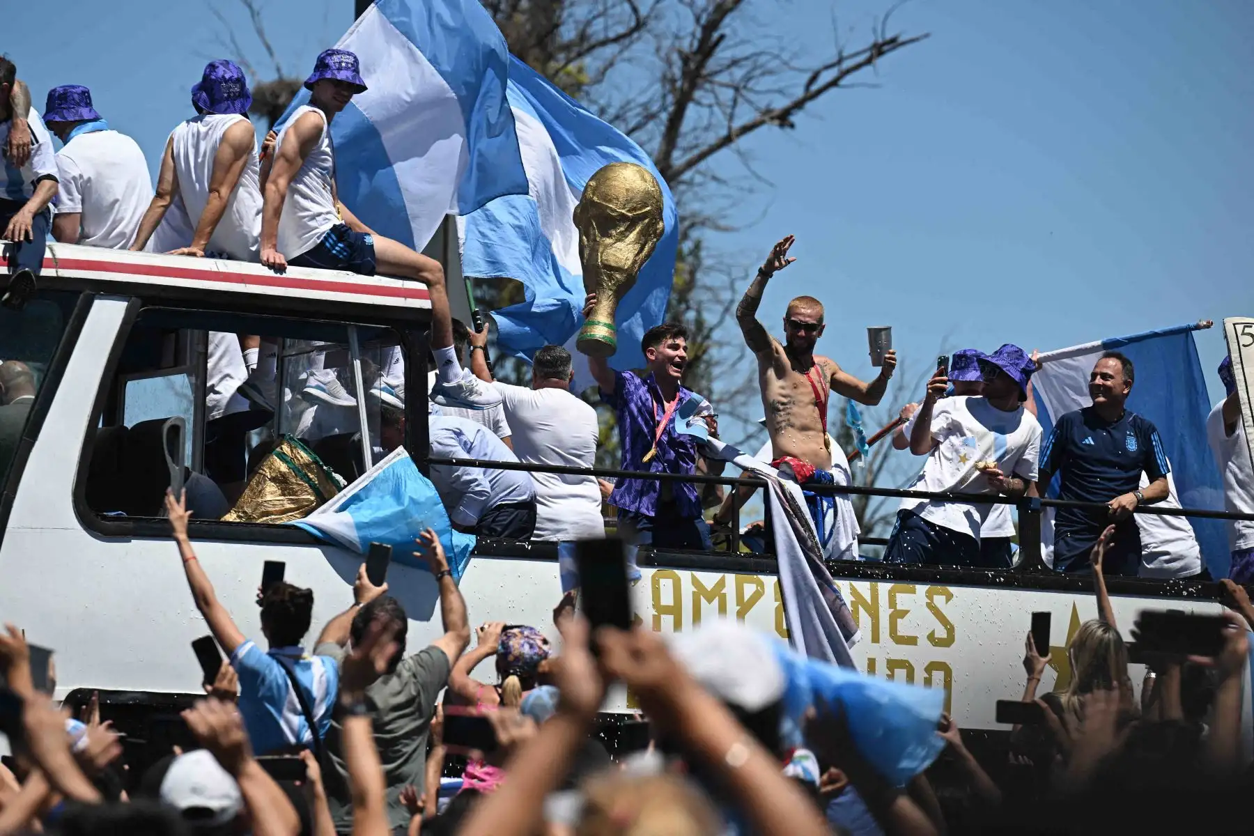 Los jugadores de Argentina celebran a bordo de un autobús con un cartel que dice "Campeones del mundo" con los seguidores después de ganar el torneo de la Copa del Mundo de Qatar 2022 mientras recorren el centro de Buenos Aires el 20 de diciembre de 2022. Se espera que millones de fanáticos exultantes animen a sus héroes Mientras los ganadores de la Copa del Mundo de Argentina, encabezados por el capitán Lionel Messi, comenzaron su desfile de autobuses descubiertos en la capital, Buenos Aires, el martes, lu