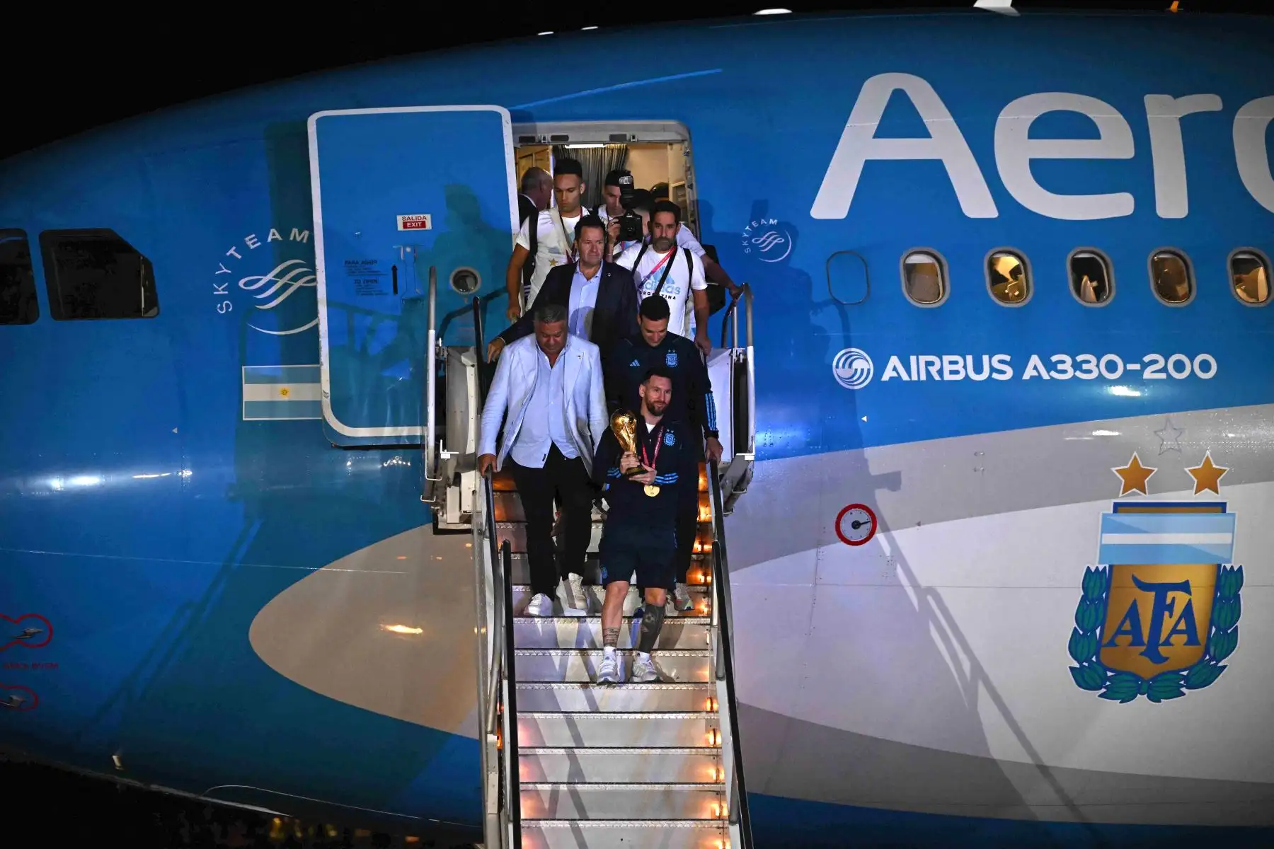 El capitán y delantero argentino Lionel Messi (C) sostiene el Trofeo de la Copa Mundial de la FIFA cuando baja de un avión a su llegada al Aeropuerto Internacional de Ezeiza después de ganar el torneo de la Copa Mundial de Qatar 2022 en Ezeiza, provincia de Buenos Aires, Argentina el 20 de diciembre de 2022.

Foto: AFP