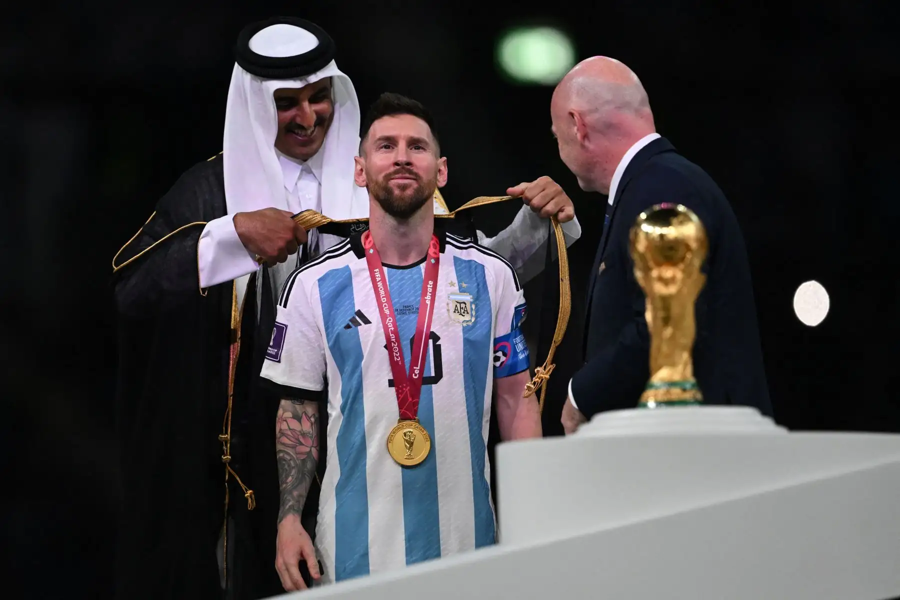El emir jeque Tamim bin Hamad al-Thani (izquierda) de Qatar envuelve una abaya alrededor del delantero argentino #10 Lionel Messi en el escenario junto al trofeo de la Copa Mundial de la FIFA después de que Argentina ganara la final de la Copa Mundial Qatar 2022 en el partido de fútbol entre Argentina y Francia en el Estadio Lusail en Lusail, al norte de Doha el 18 de diciembre de 2022.

Foto: AFP
