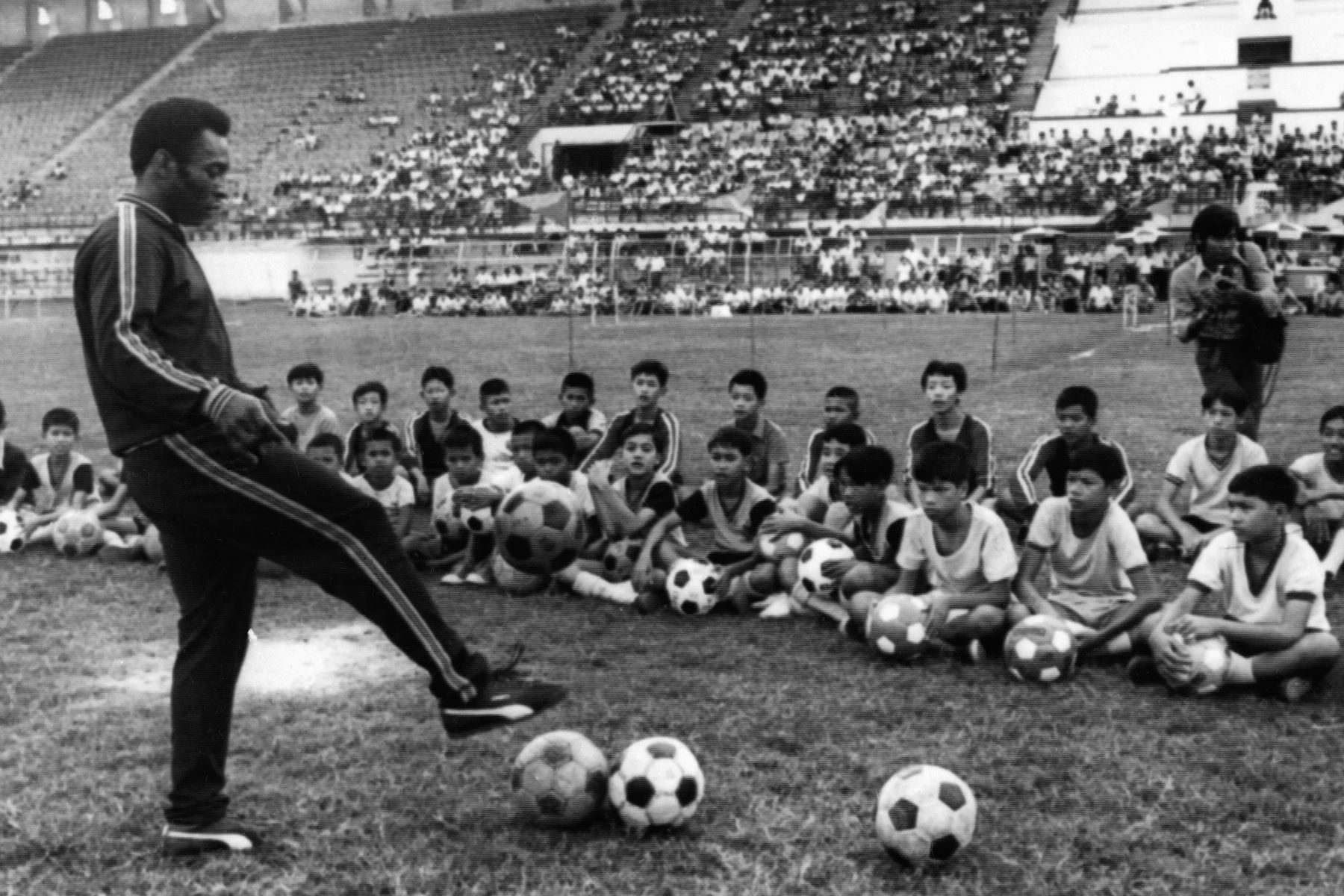 La foto tomada el 6 de diciembre de 1974 en Bangkok muestra al futbolista brasileño Pelé durante una sesión de entrenamiento con un niño como parte de un viaje comercial en Tailandia. Foto: AFP