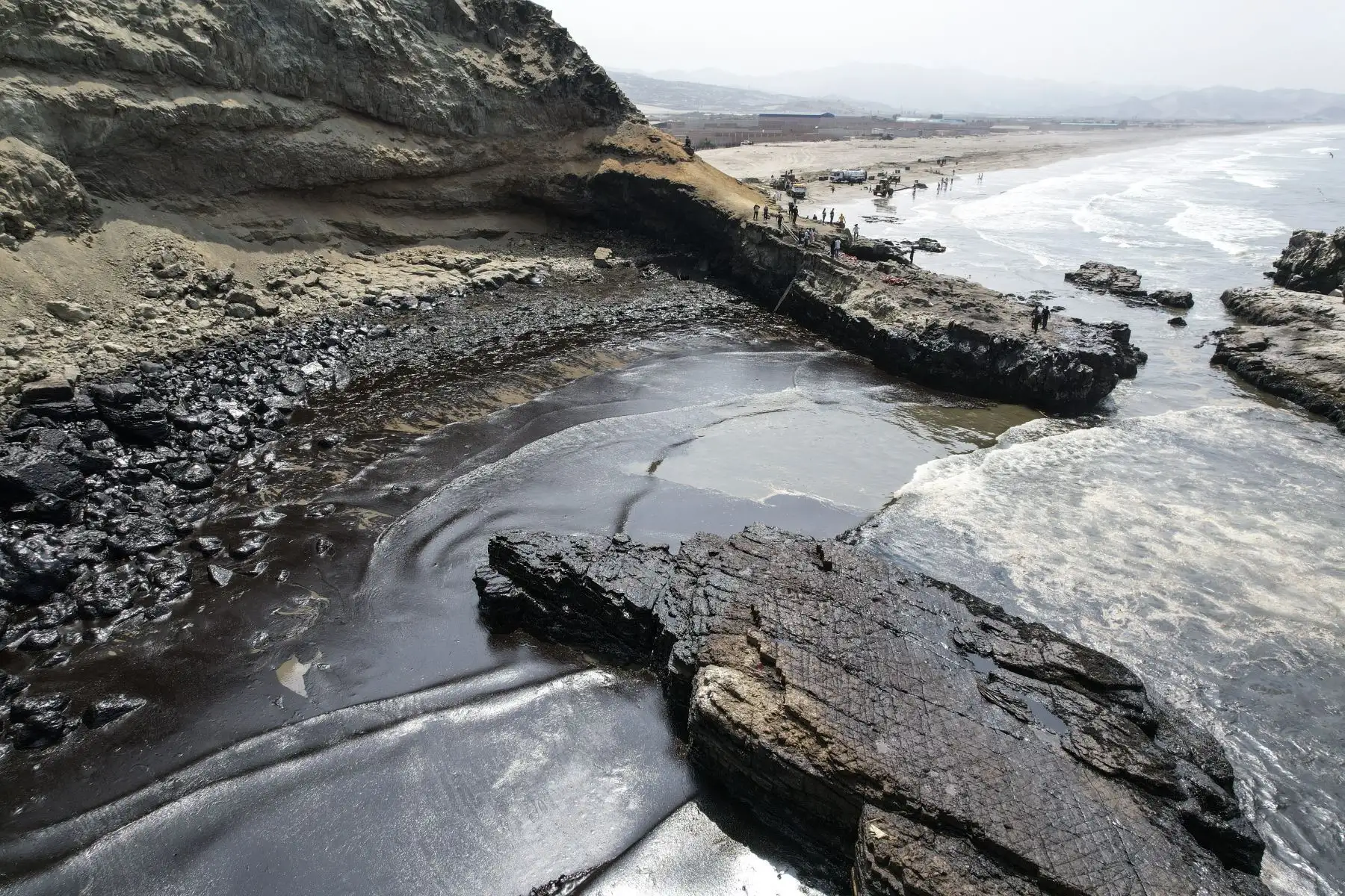 Tres operarios de una empresa contratada por Repsol intentan limpiar un sector de la playa Cavero. Tras el derrame de petróleo, la operadora de La Pampilla recibió críticas en redes sociales por enviar al lugar del desastre a trabajadores equipados apenas con escobas y recogedores domésticos. De acuerdo con las autoridades, 6,000 barriles de petróleo terminaron en el mar. Foto: ANDINA/Jhonel Rodríguez Robles