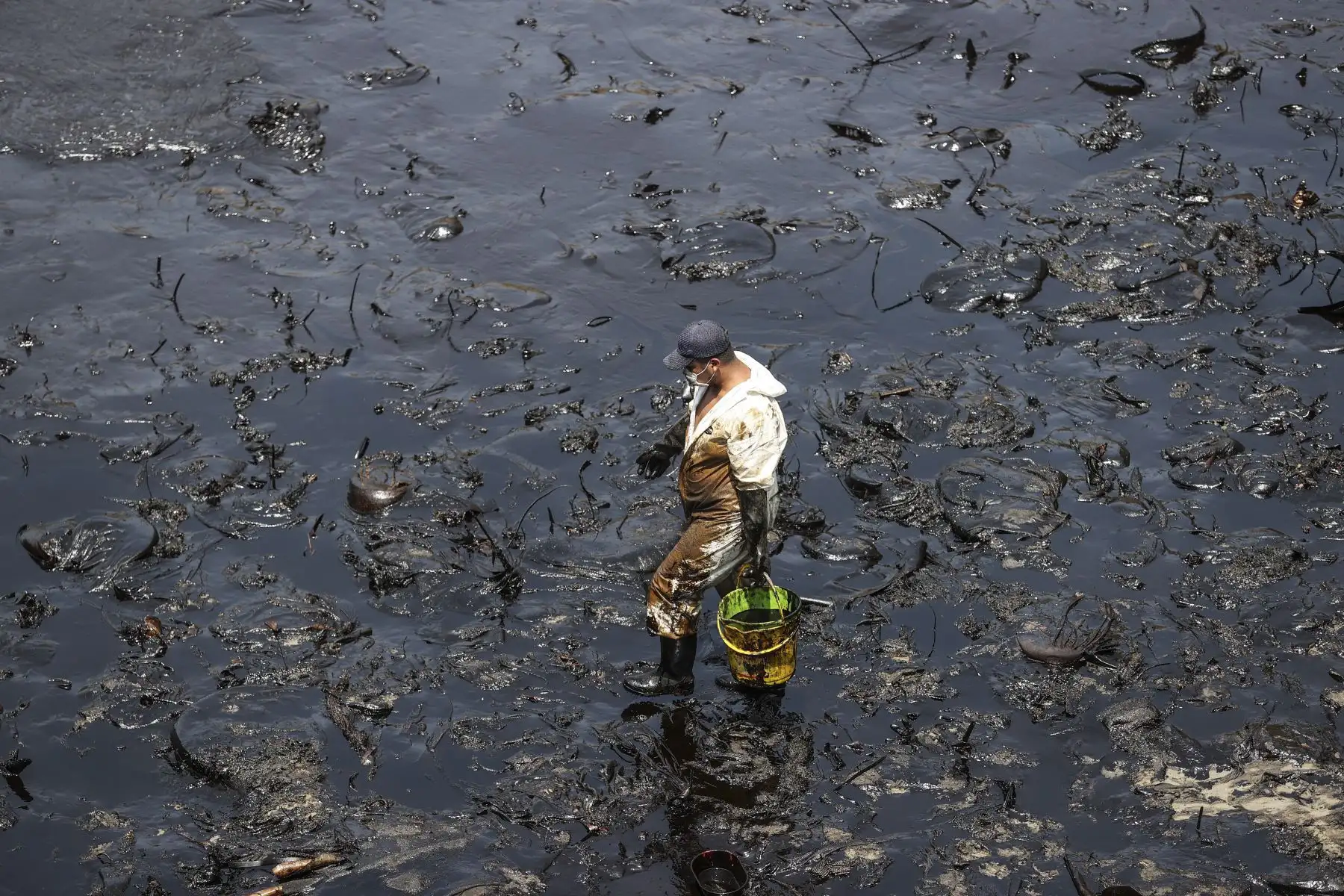 Con un balde plástico de 5 galones, un trabajador se abre paso en la playa Cavero, inundada por el petróleo que cayó al mar el sábado 15 de enero. De acuerdo con las autoridades, alrededor de 6,000 barriles de petróleo terminaron en el mar, pese a que inicialmente la empresa Repsol dijo que solo cayeron 6 galones desde un buque de bandera italiana. Foto: ANDINA/Jhonel Rodríguez Robles