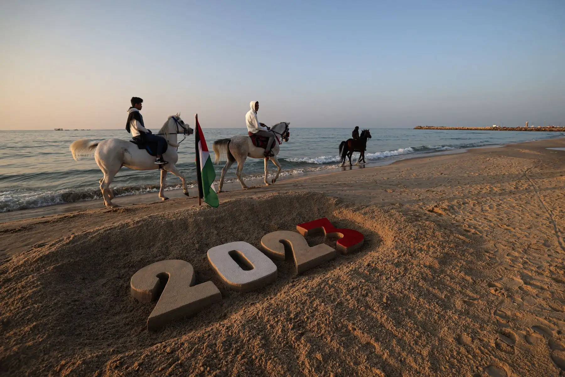 Los palestinos montan a caballo frente a una creación de arena que dice "2023" en una playa, en la ciudad de Gaza, el 31 de diciembre de 2022, durante la última puesta de sol de 2022. Foto: AFP