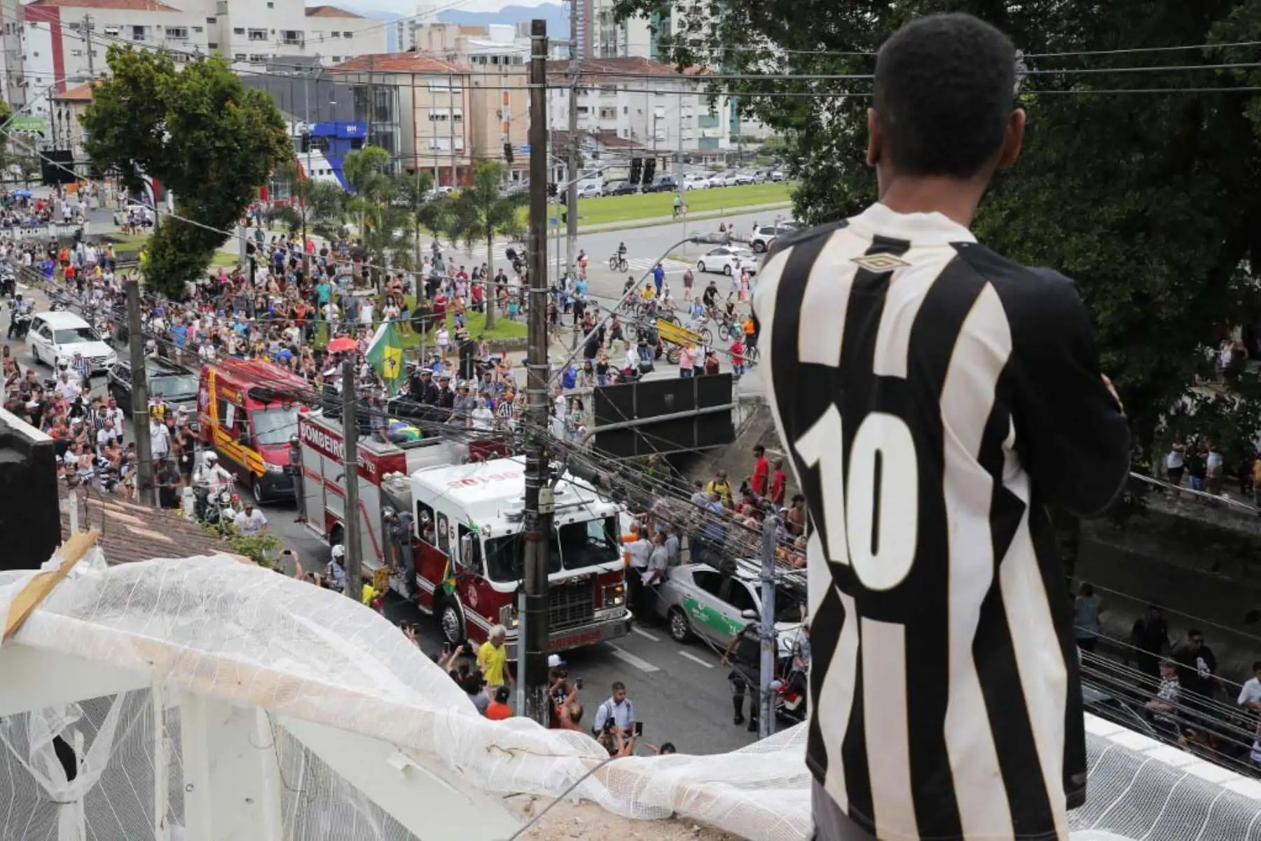 Un fanático de la fallecida estrella del fútbol brasileño Pelé observa desde un techo como un camión de bomberos transporta el ataúd de Pelé al Cementerio Conmemorativo de Santos en Santos, estado de Sao Paulo, Brasil. Foto: AFP