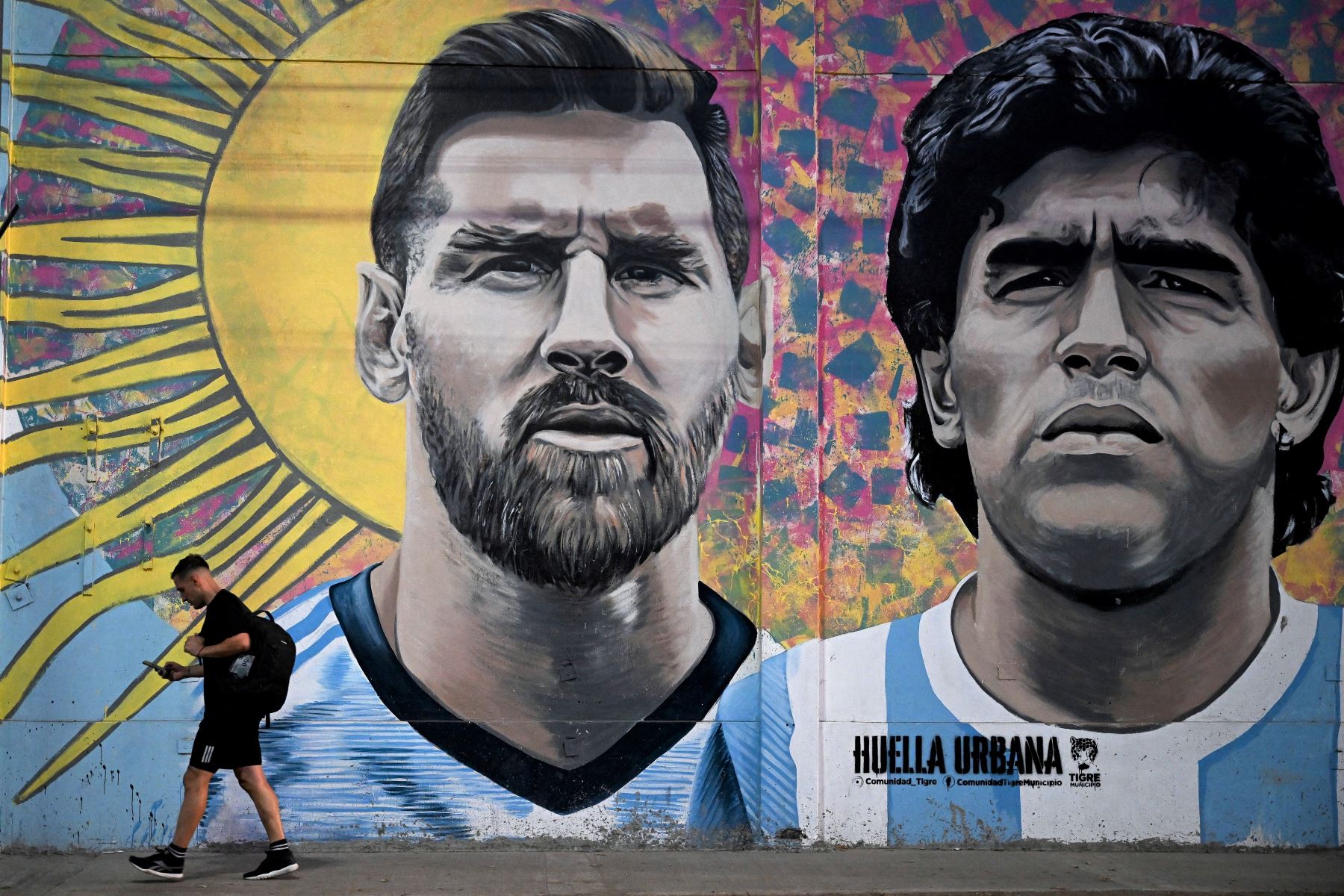 Un transeúnte pasa junto a un mural que representa a las estrellas del fútbol argentino Lionel Messi y  Diego Maradona, en diciembre de 2022. Foto: AFP.