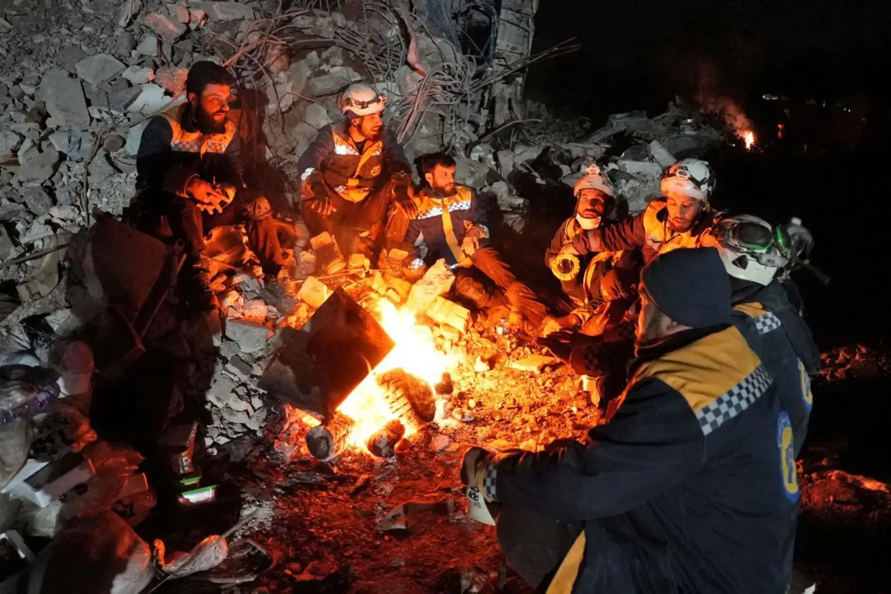 Miembros de la defensa civil siria, conocidos como los Cascos Blancos, se calientan junto a un fuego junto a los escombros de un edificio derrumbado, en la ciudad de Jandairis. Foto: AFP