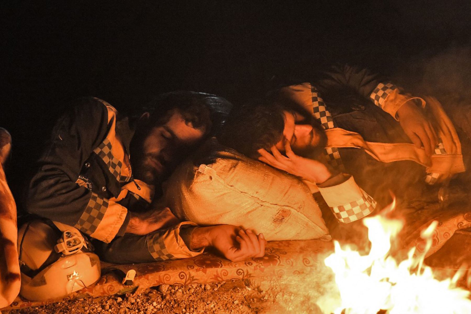 Miembros de la defensa civil siria, conocidos como Cascos Blancos, duermen junto a un incendio en la ciudad de Jandairis. Foto: AFP