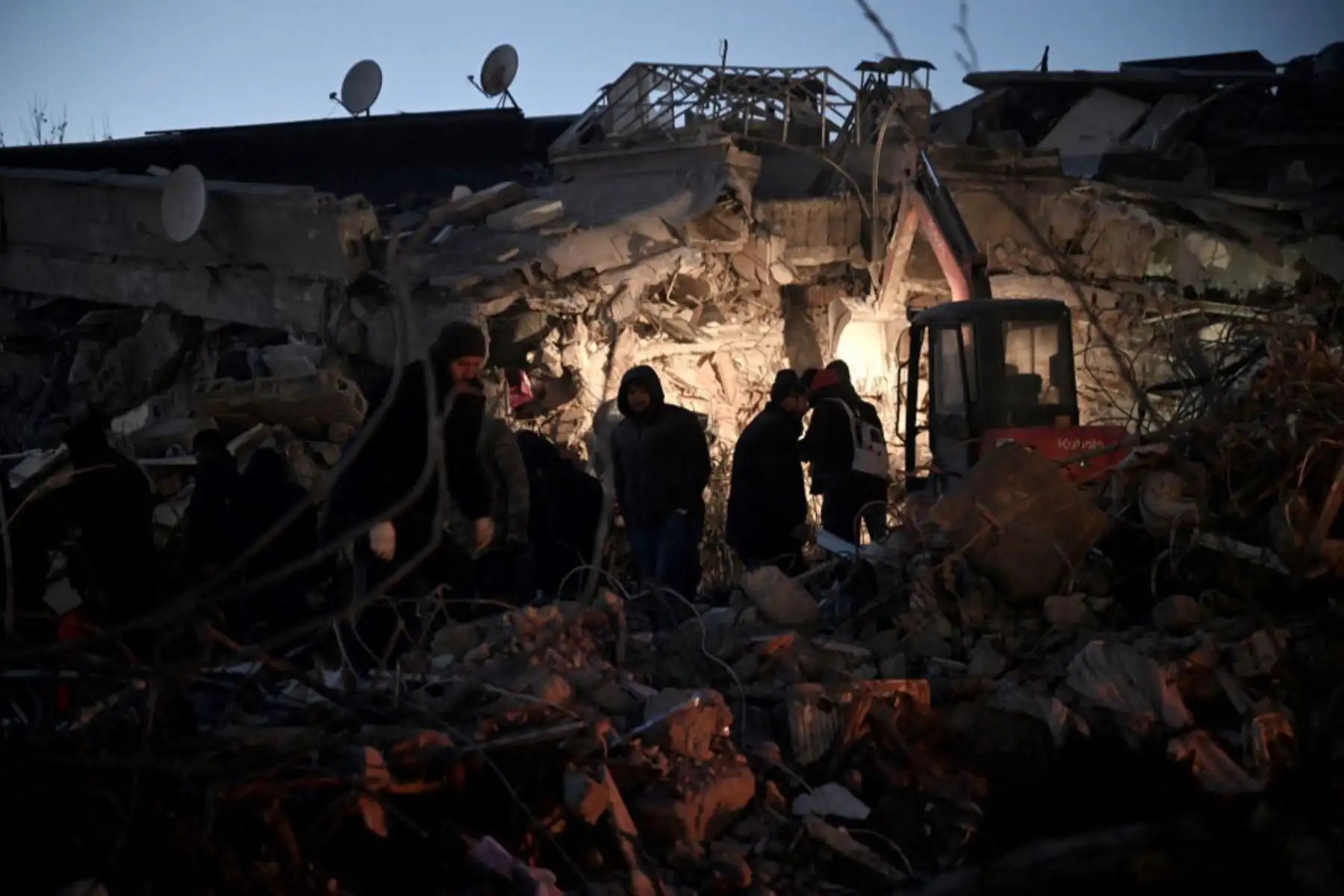 Miembros de la defensa civil siria, se calientan junto a un fuego junto a los escombros de un edificio derrumbado por el terremoto. Foto: AFP