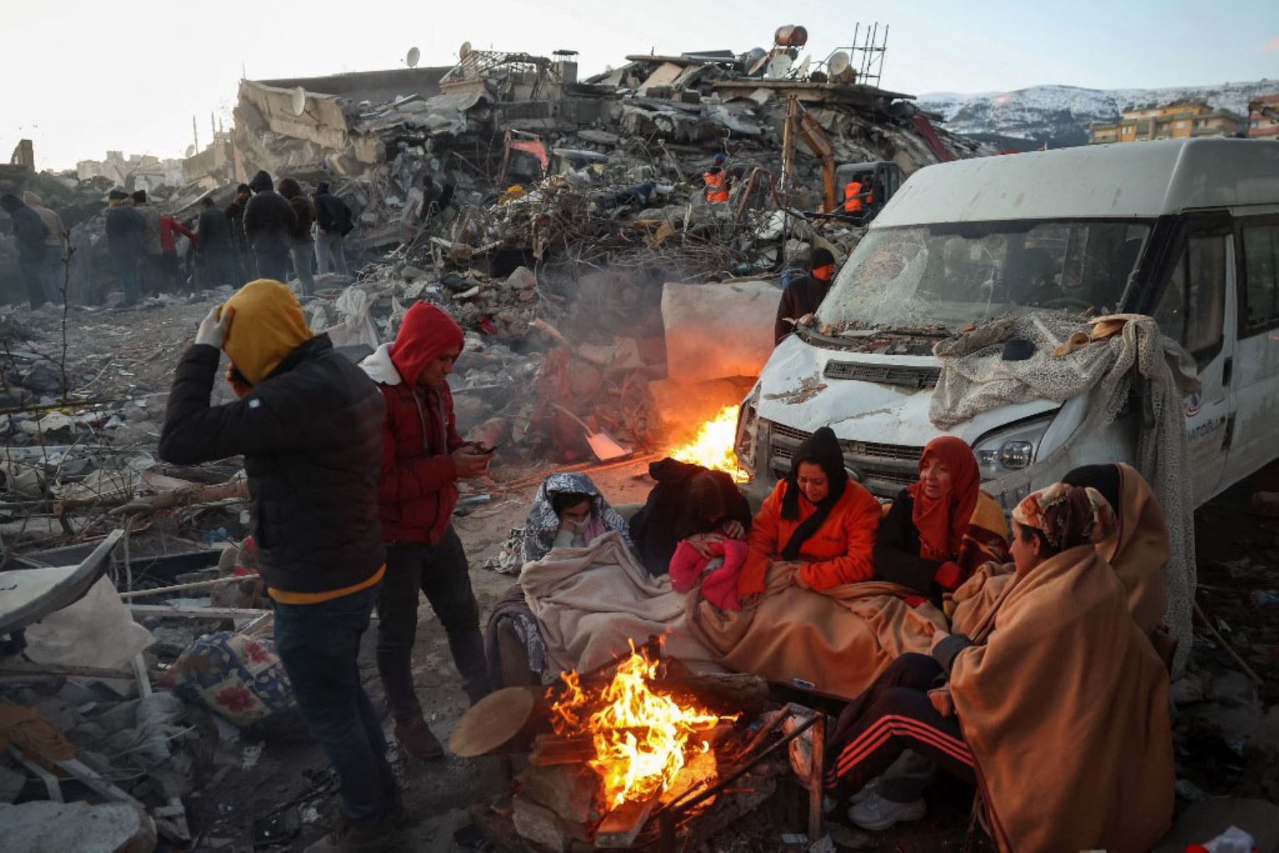 Familias se calientan junto a un fuego junto a los escombros de un edificio derrumbado por el terremoto. Foto: AFP