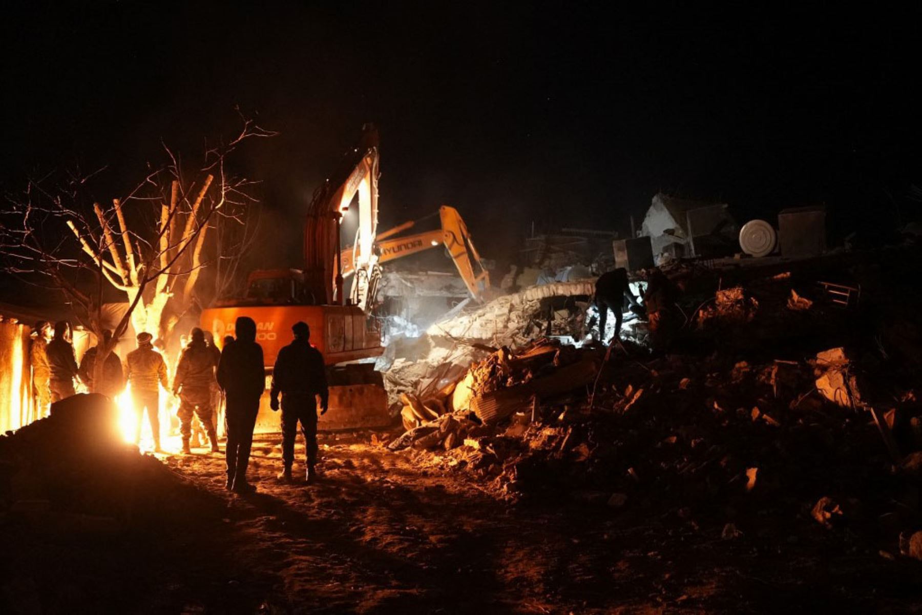 Miembros de la defensa civil siria, se calientan junto a un fuego junto a los escombros de un edificio derrumbado por el terremoto. Foto: AFP