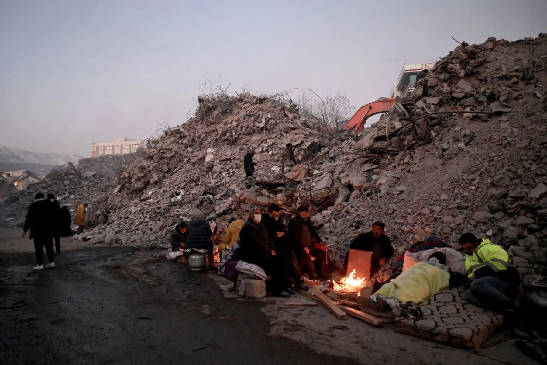Familiares se calientan alrededor de un fuego frente a los escombros de los edificios derrumbados mientras los equipos de rescate continúan buscando víctimas y sobrevivientes. Foto: AFP