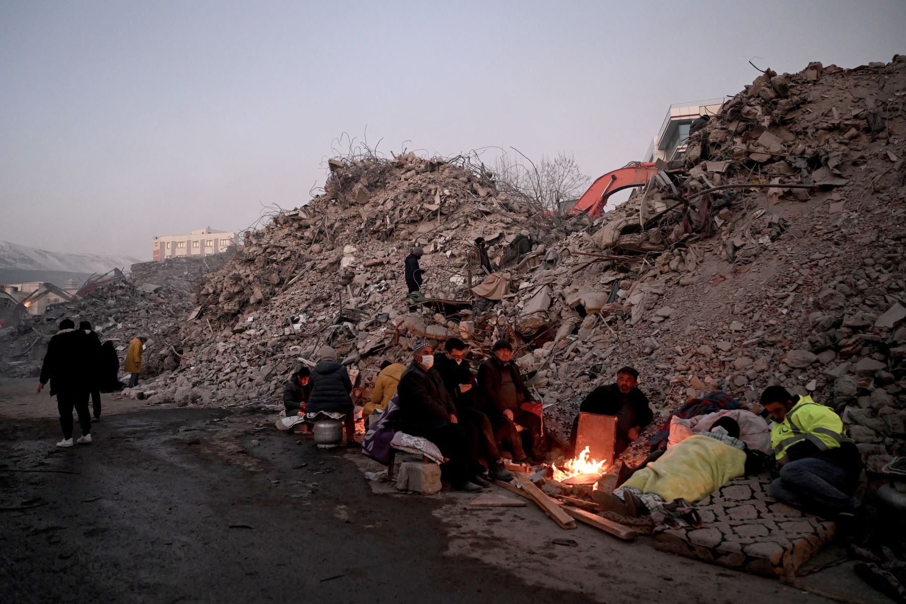 Los familiares se calientan alrededor de una fogata frente a los escombros de edificios derrumbados mientras los equipos de rescate continúan buscando víctimas y sobrevivientes, luego de que un terremoto de magnitud 7.8 azotara la región fronteriza de Turquía y Siria en Kahramanmaras. Foto: AFP/Archivo