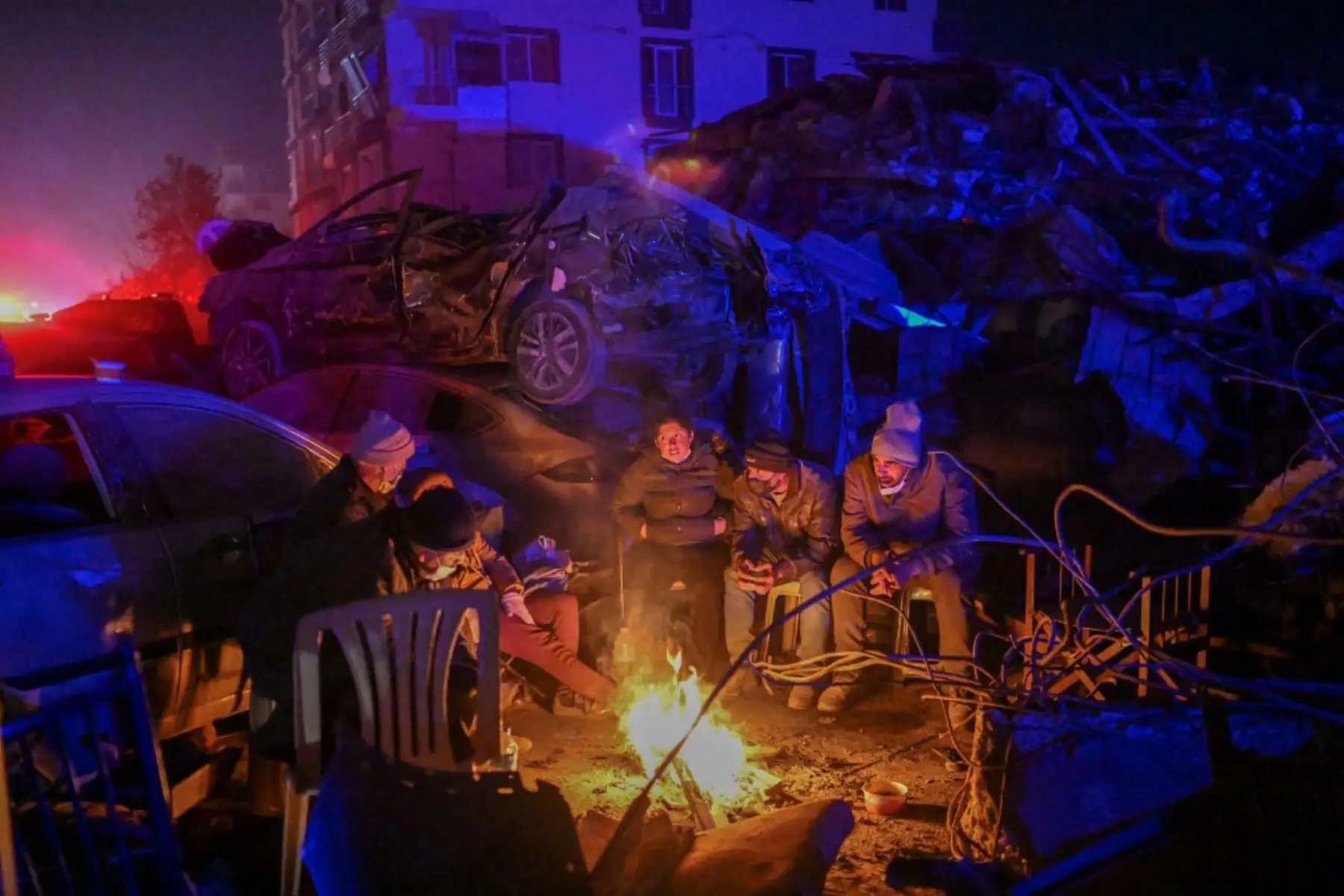 Las personas se sientan junto a una fogata, esperando noticias de sus familiares entre los escombros de los edificios derrumbados en Hatay. Foto: AFP