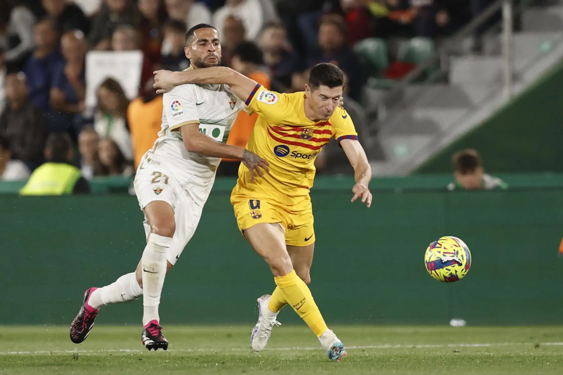 El delantero polaco del FC Barcelona, Robert Lewandowski (d), intenta llevarse el balón ante el acoso del centrocampista del Elche, Omar Mascarell, durante el encuentro correspondiente a la jornada 27 de LaLiga Santander disputado hoy sábado en el estadio Manuel Martinez Valero de la localidad alicantina. Foto: EFE
