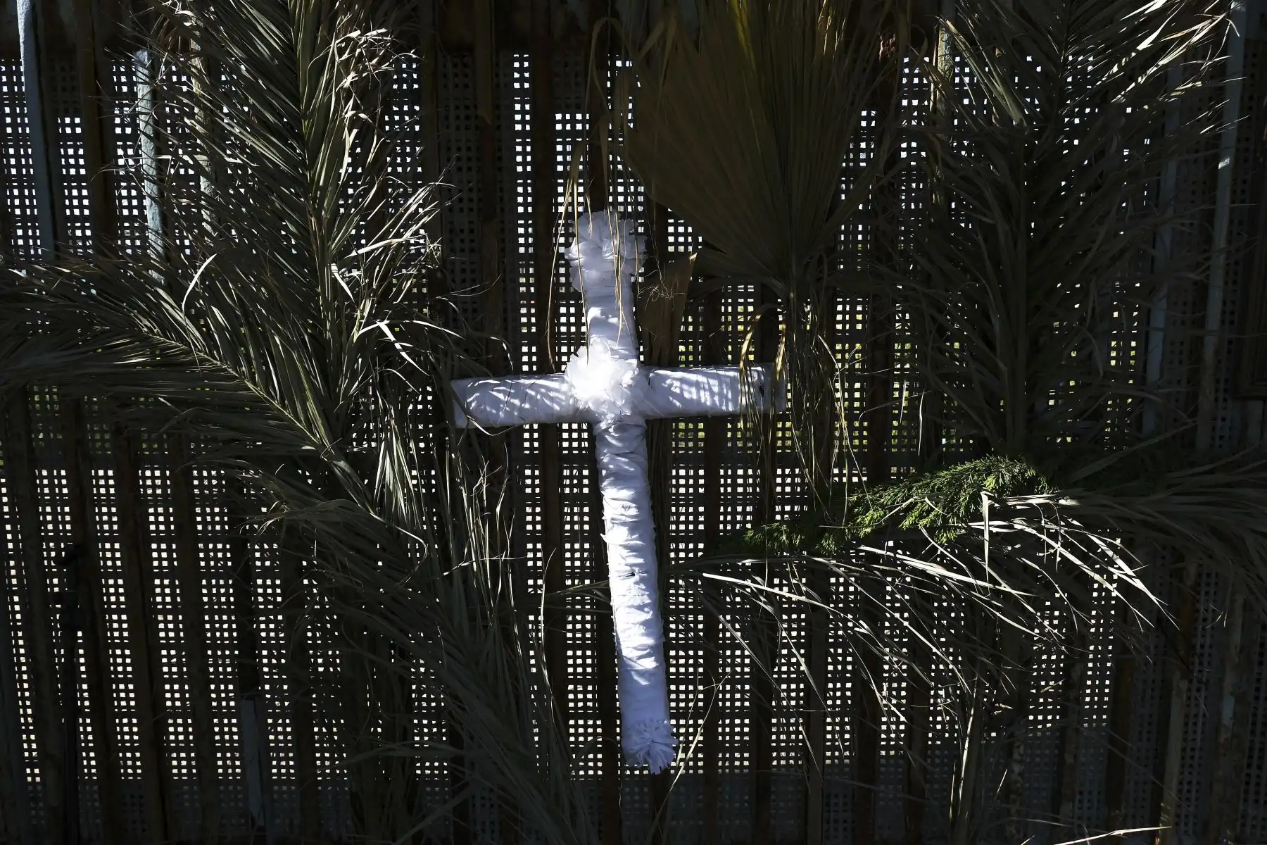 Una cruz y palmas cuelgan del muro fronterizo mientras defensores y activistas participan de una ceremonia de Semana Santa en el Parque de la Amistad en la frontera entre México y EE. UU. en Playas de Tijuana, estado de Baja California, México. Foto: AFP