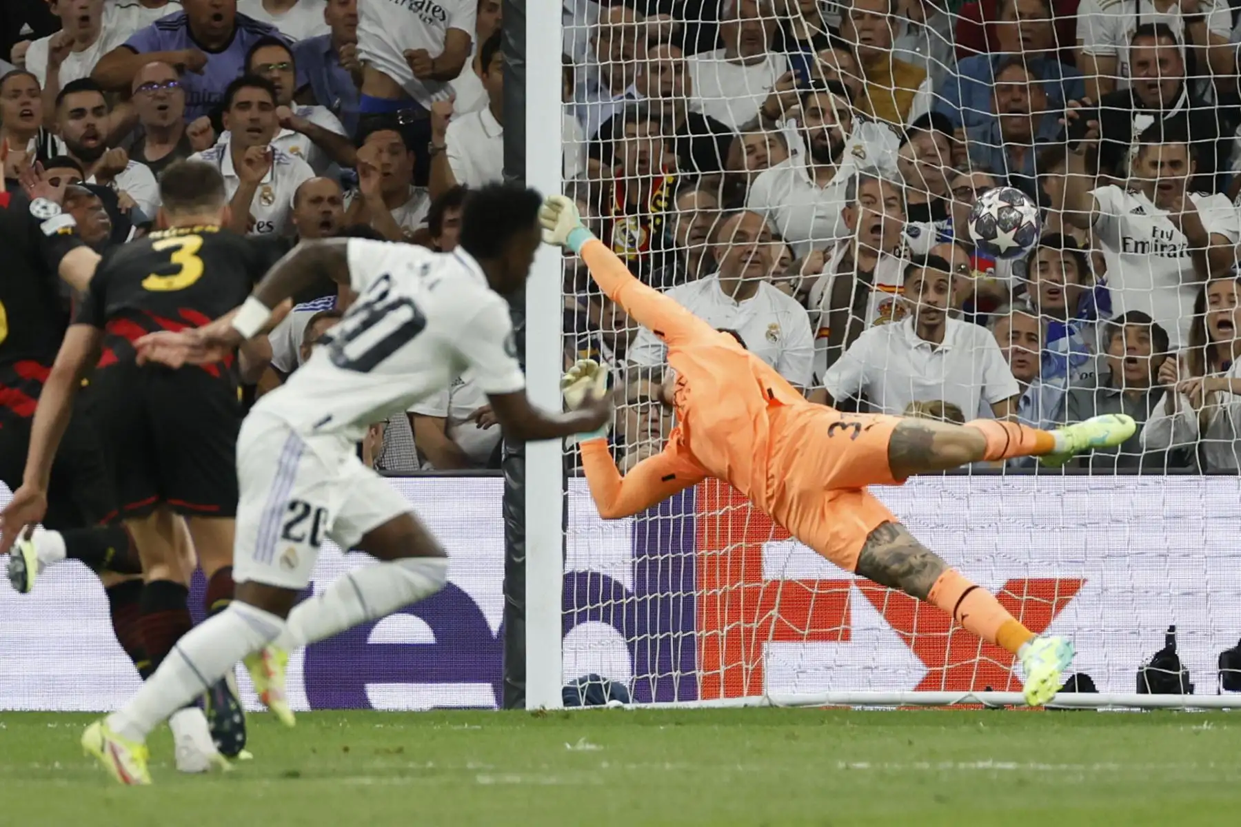El guardameta brasileño del Manchester City, Ederson (d), intenta detener el balón golpeado por el delantero brasileño del Real Madrid, Vinicius Jr. y que ha significado el primer gol del equipo madridista durante el encuentro correspondiente a la ida de las semifinales de la Liga de Campeones que disputan hoy martes en el estadio Santiago Bernabéu, en Madrid.
Foto: EFE