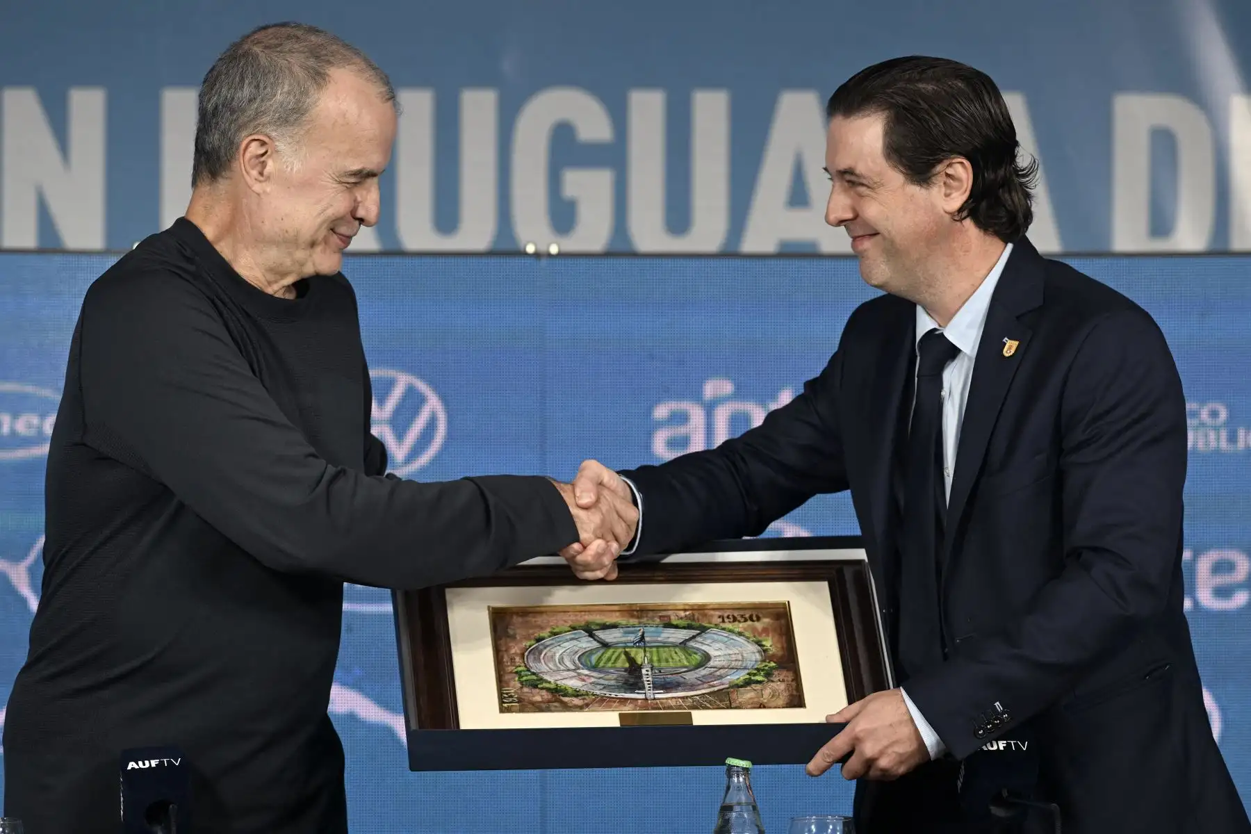 El argentino Marcelo Bielsa recibe un obsequio del presidente de la Asociación Uruguaya de Fútbol (AUF), Ignacio Alonso, durante su presentación como entrenador de la selección uruguaya de fútbol, ​​en el Estadio Centenario de Montevideo, el 17 de mayo de 2023. 
Foto: AFP