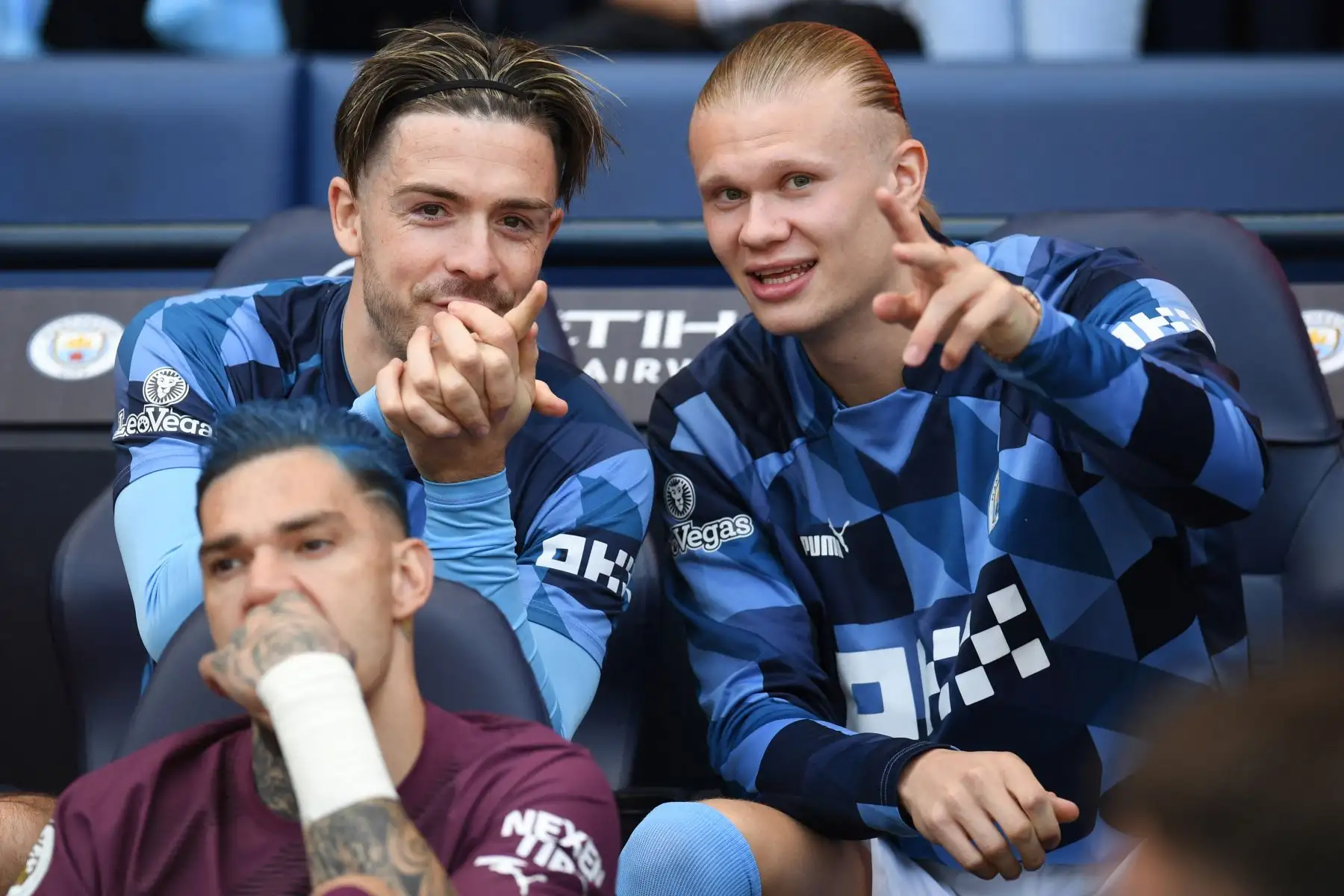 El mediocampista inglés del Manchester City, Jack Grealish, habla con el delantero noruego del Manchester City, Erling Haaland, mientras se sientan en el banco con el portero brasileño del Manchester City, Ederson, durante el partido de fútbol de la Premier League inglesa entre el Manchester City y el Chelsea. Foto:ANDINA/ AFP