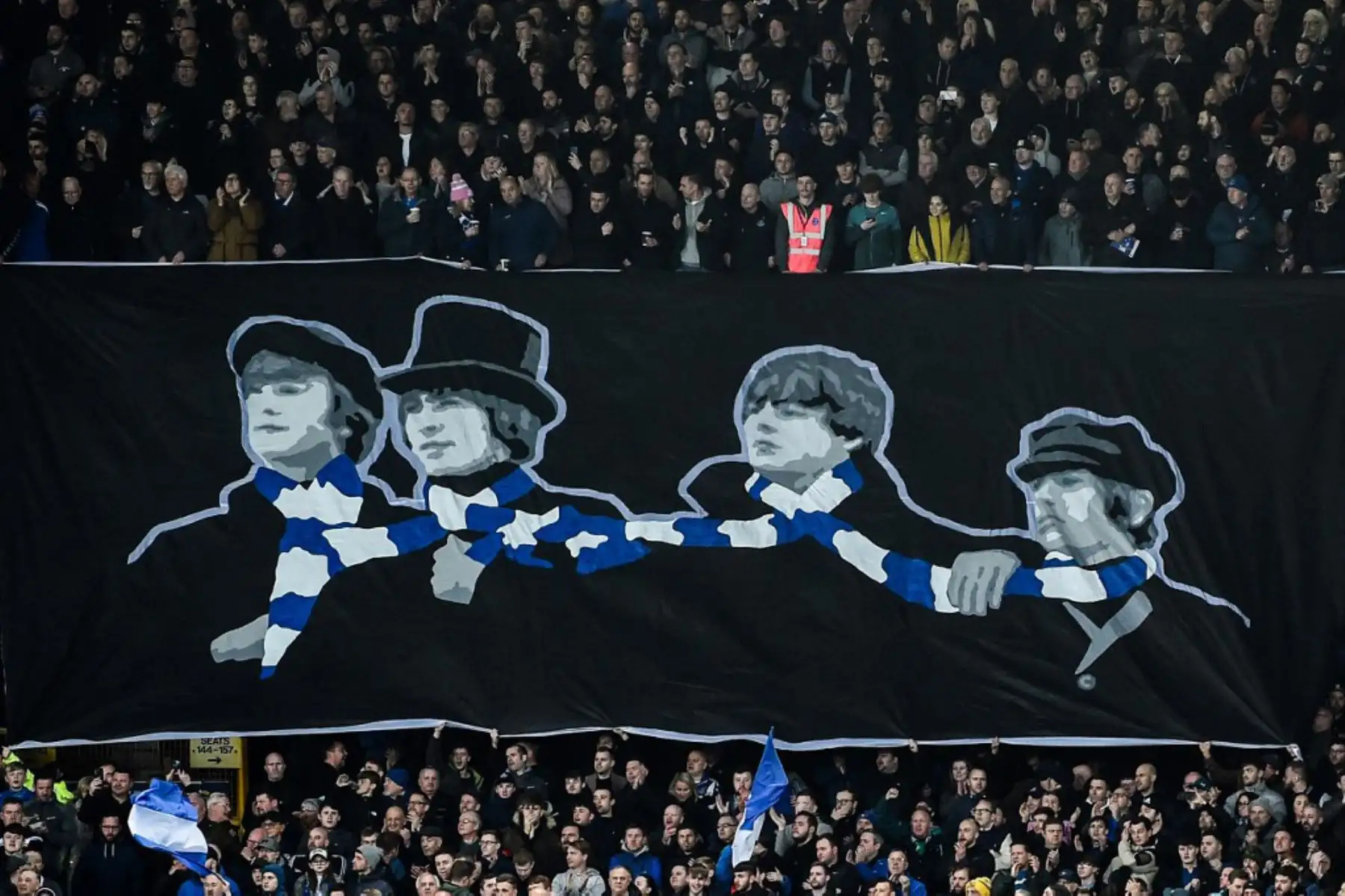 Seguidores sostienen una pancarta que muestra a los Beatles con la bufanda del Everton durante el partido de fútbol de la Premier League inglesa en Liverpool. Foto: AFP