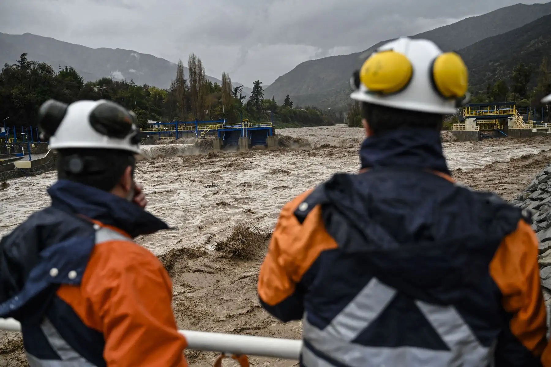 Técnicos de la empresa Aguas Andinas observan una presa de captación de agua en el río Maipo en San José de Maipo, Santiago, Chile el 23 de junio de 2023. Las fuertes lluvias están afectando la zona central de Chile, provocando el desbordamiento de varios ríos creando inundaciones, apagones y suspensión de las clases escolares.
Foto: AFP