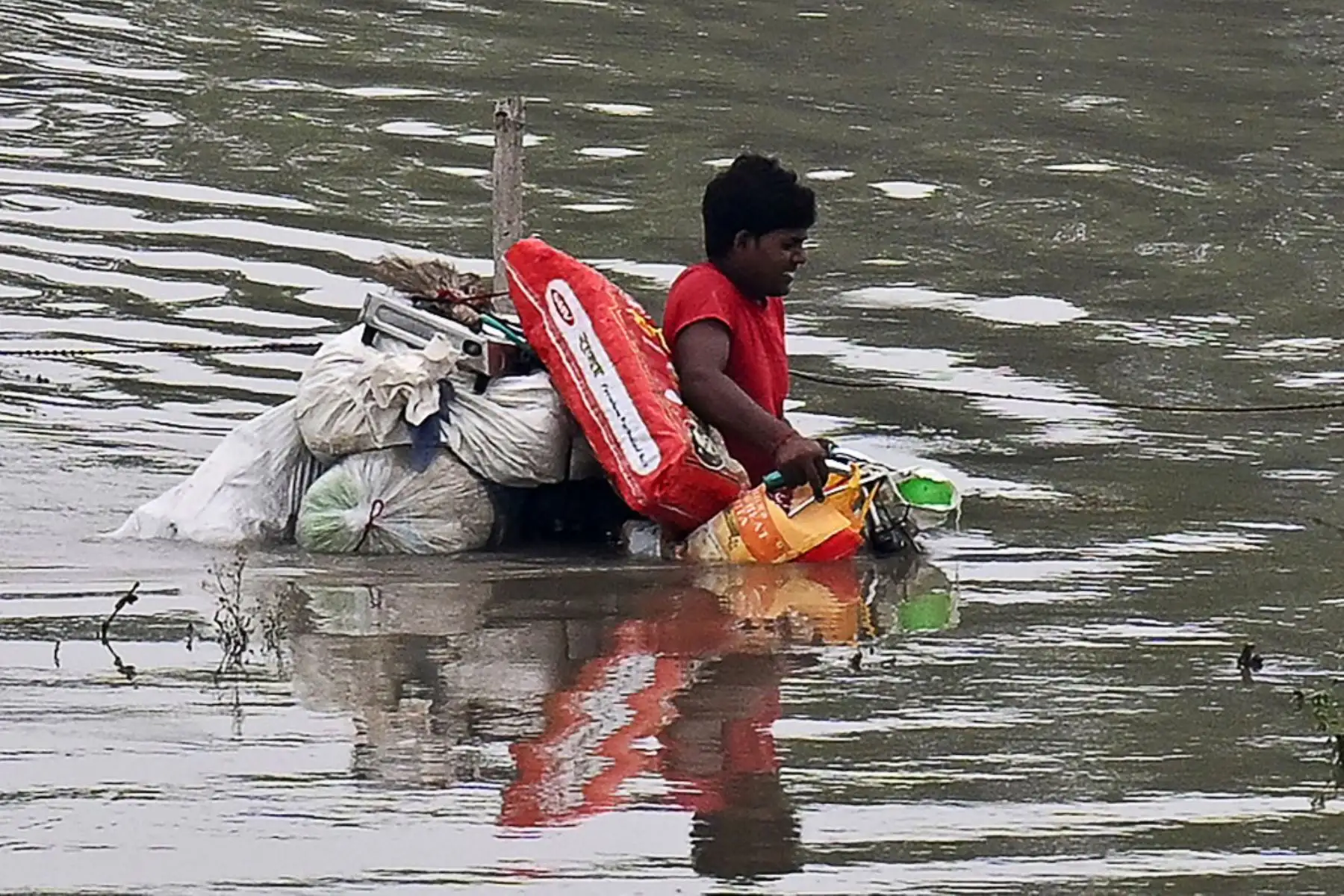 Un hombre empuja una bicicleta cargada con sus pertenencias en una zona baja inundada cerca del río Yamuna después de que se desbordara debido a las lluvias monzónicas en Nueva Delhi. Foto: AFP