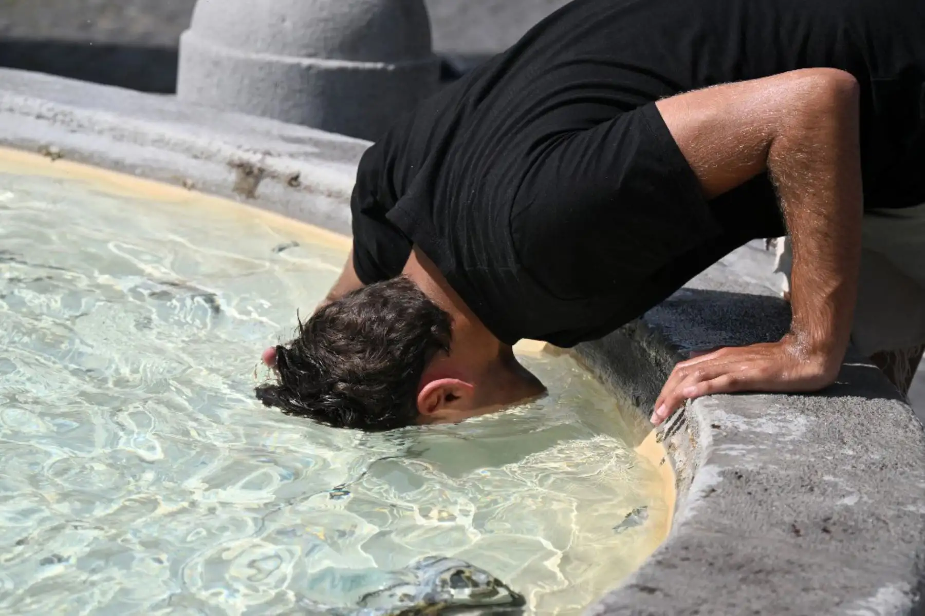 Un hombre mete la cabeza en el agua para refrescarse en la fuente de la Piazza del Popolo en Roma. Foto: AFP